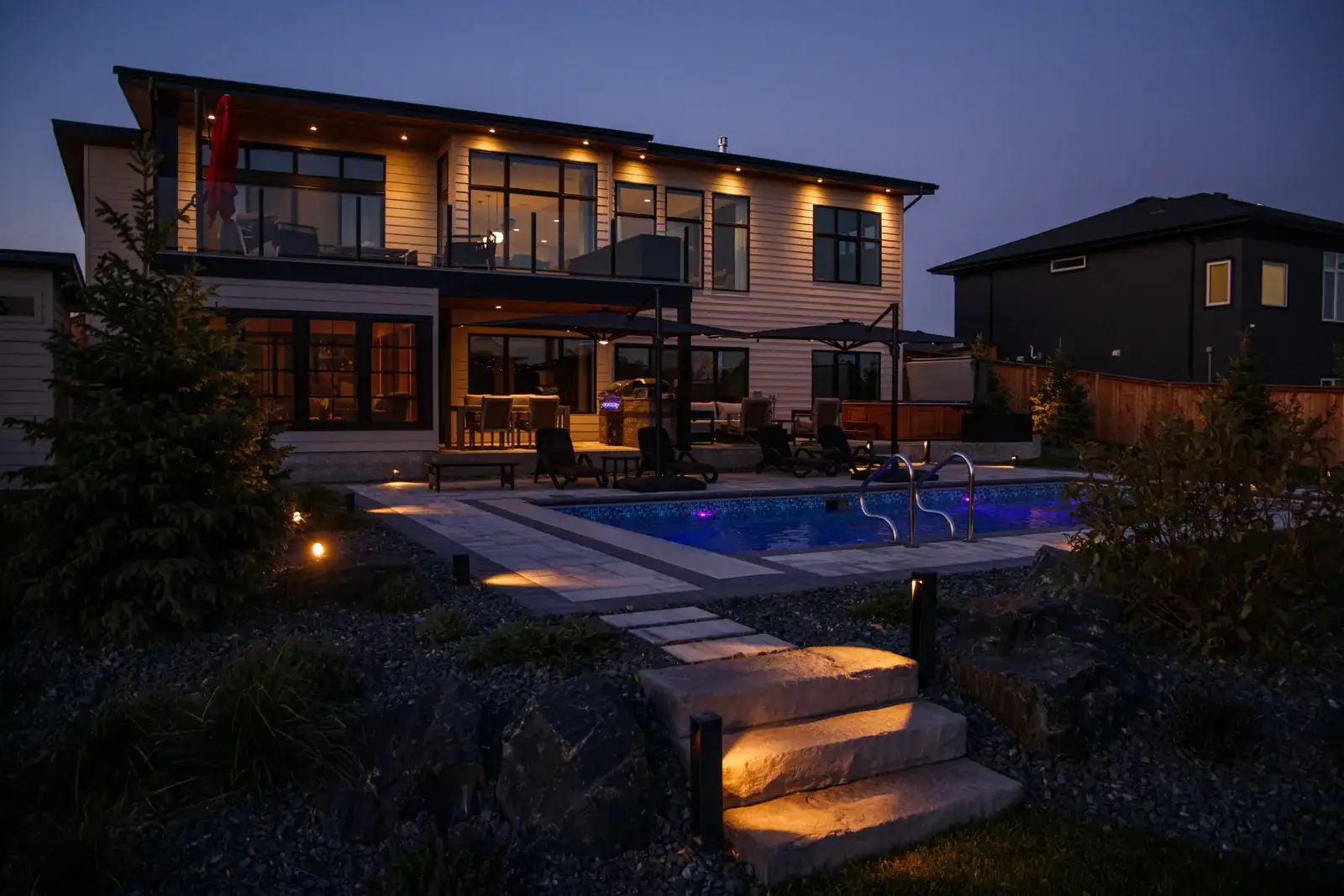 Modern house and backyard pool with landscape lighting at dusk