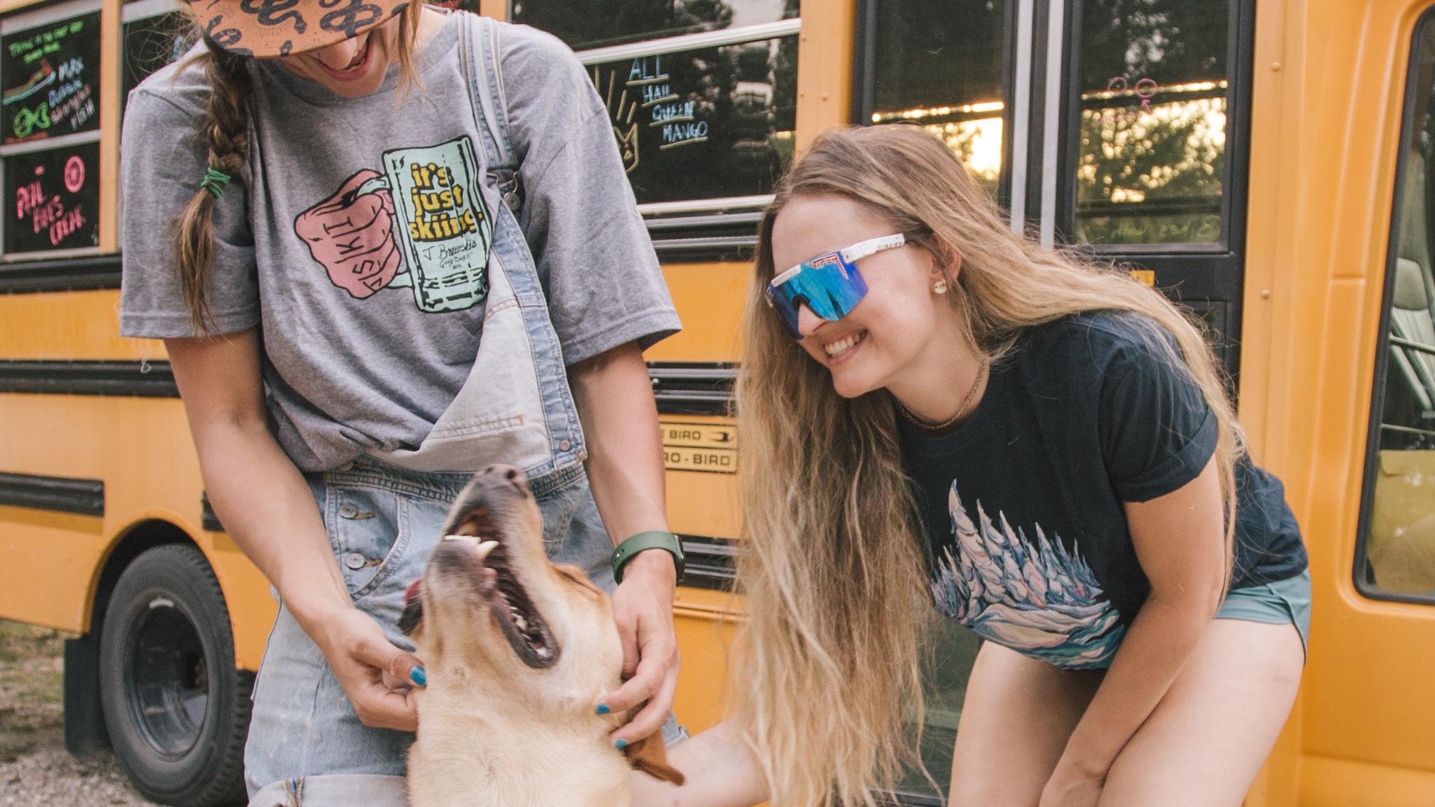 Two girls wearing J skis t-shirts petting a happy dog