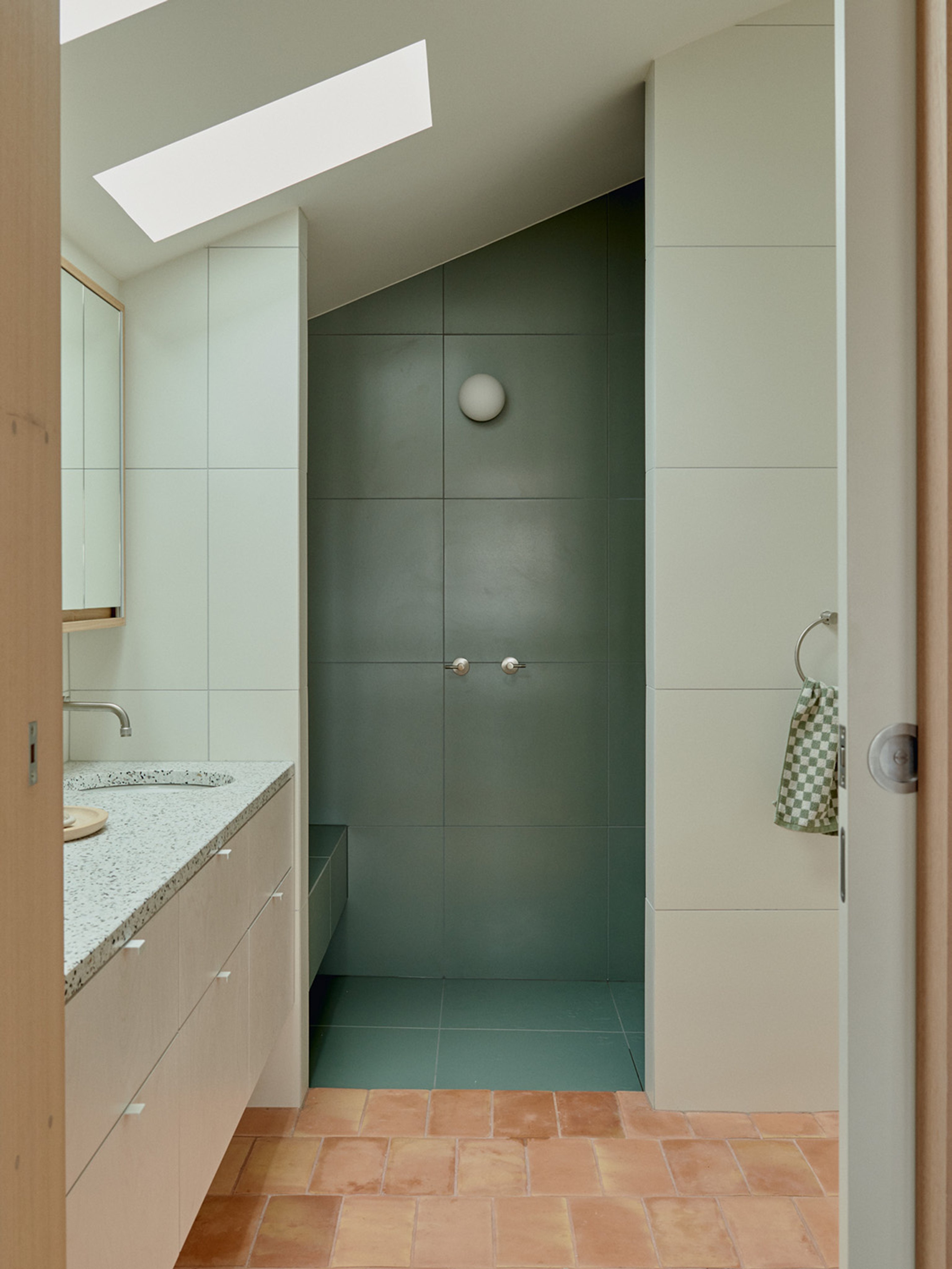 A bathroom with terracotta floor tiles, a green tiled shower and skylights, letting in natural light