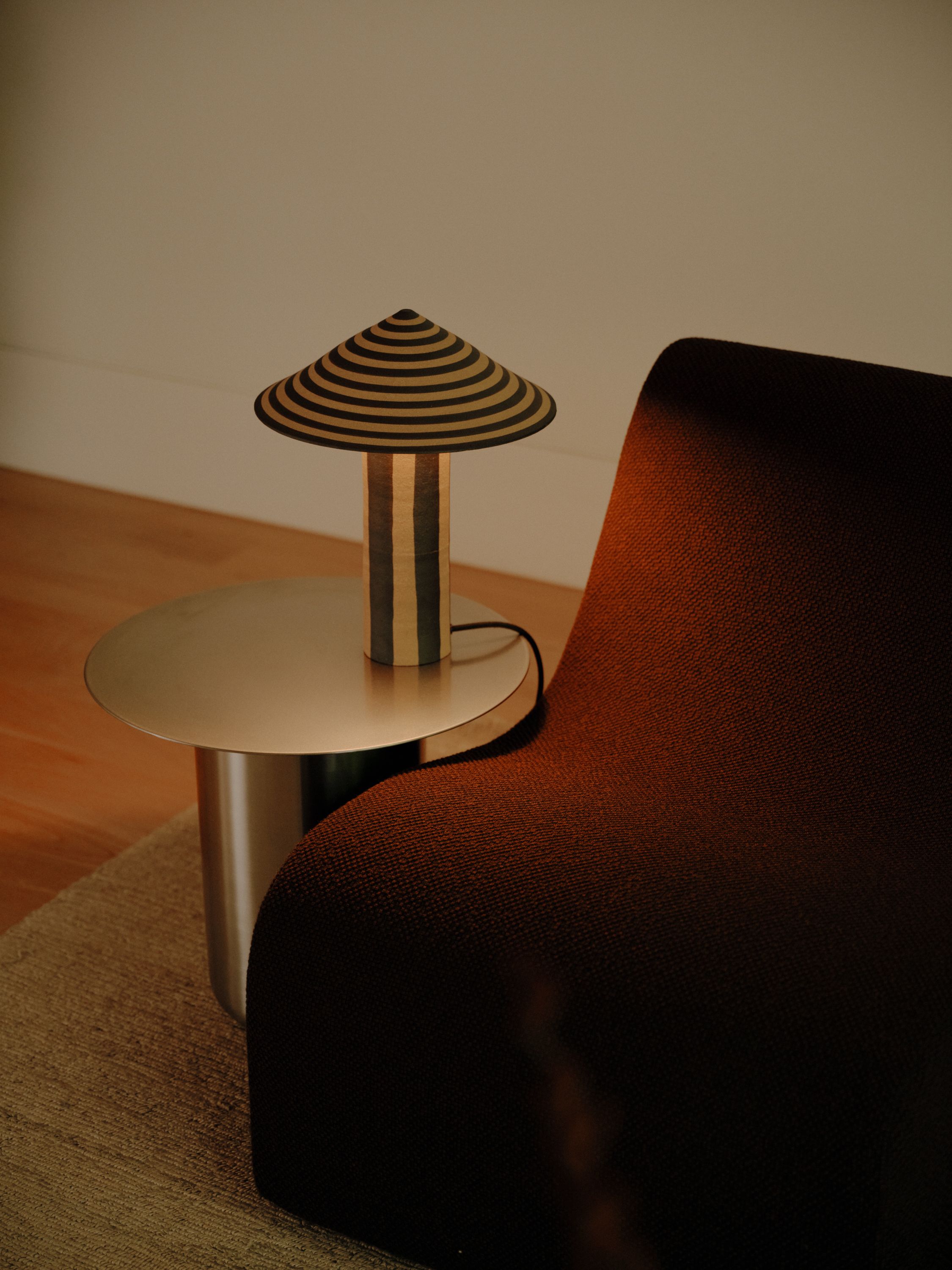 A striped ceramic Dancer Table Lamp sits on a Stainless Steel Sequence 01 Side Table, next to a purple Monde modular sofa