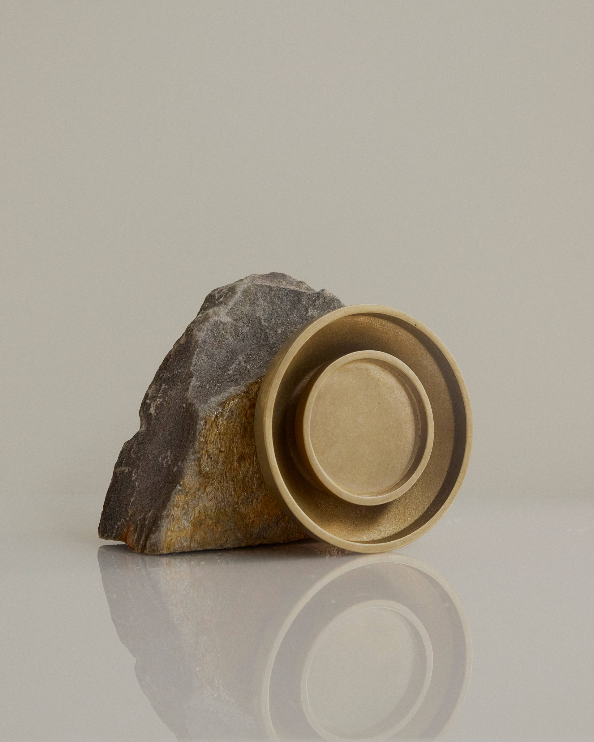 Chorus Wall Light in Brass, resting against a large rock.