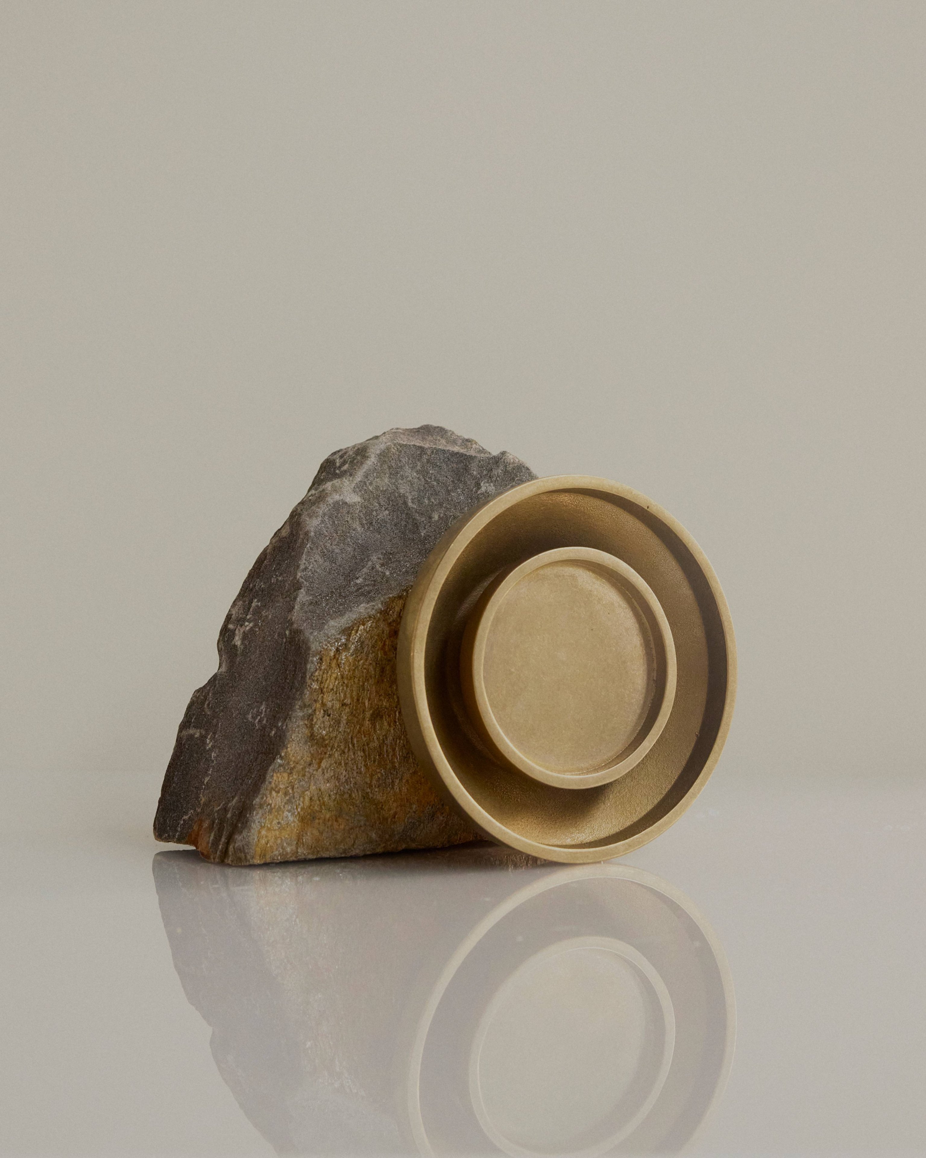 Chorus Wall Light in Brass, resting against a large rock.