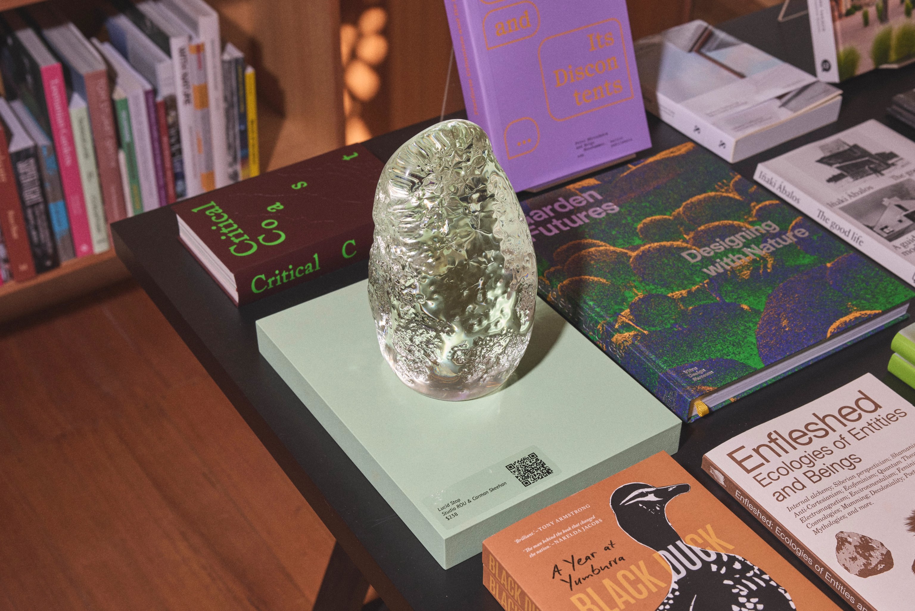 A transparent clear glass sculpture sitting on a collection of books