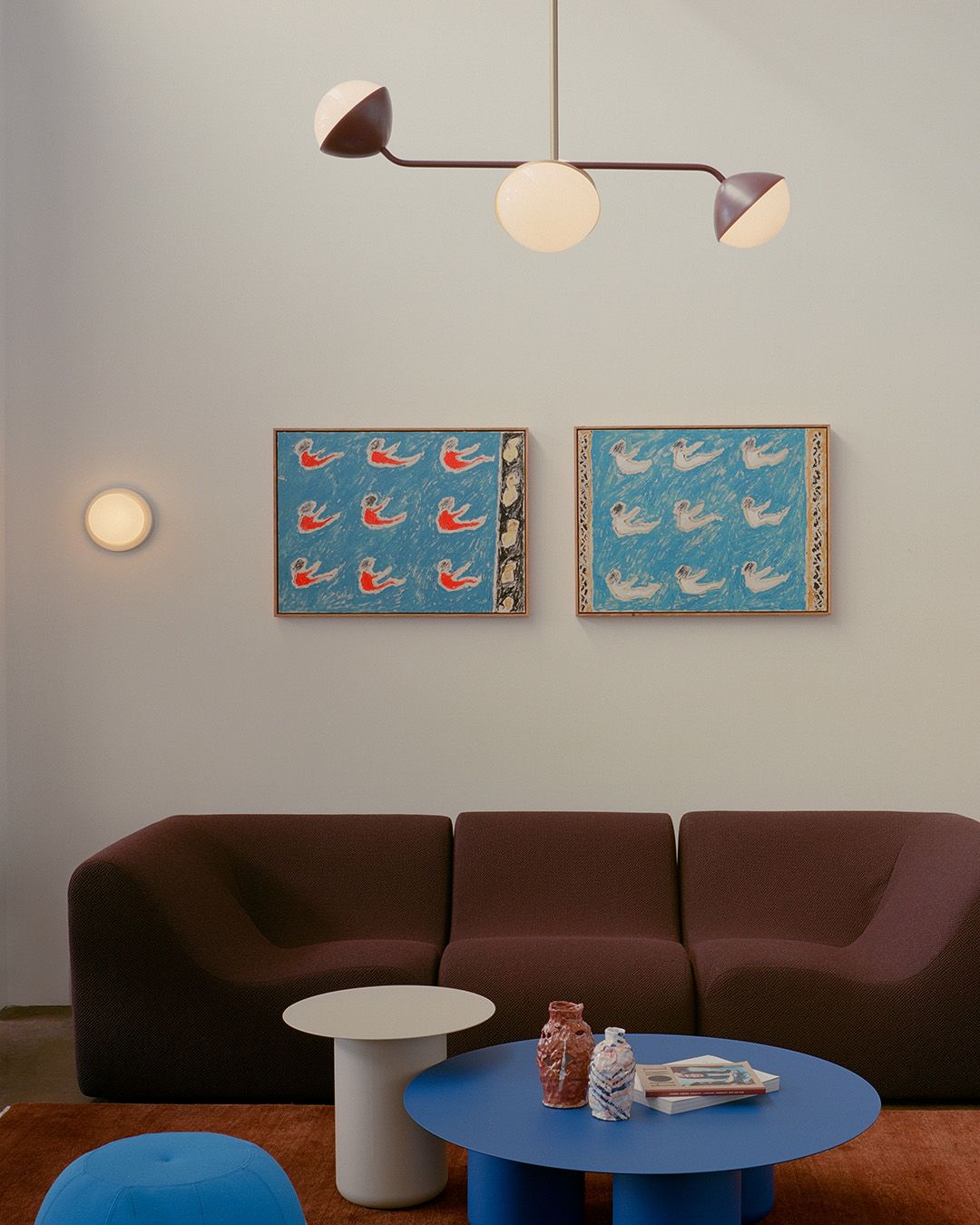 Jolly double rod pendants in the Coco Flip showroom above a burgundy sofa. The room has white walls, artwork and colourful coffee table