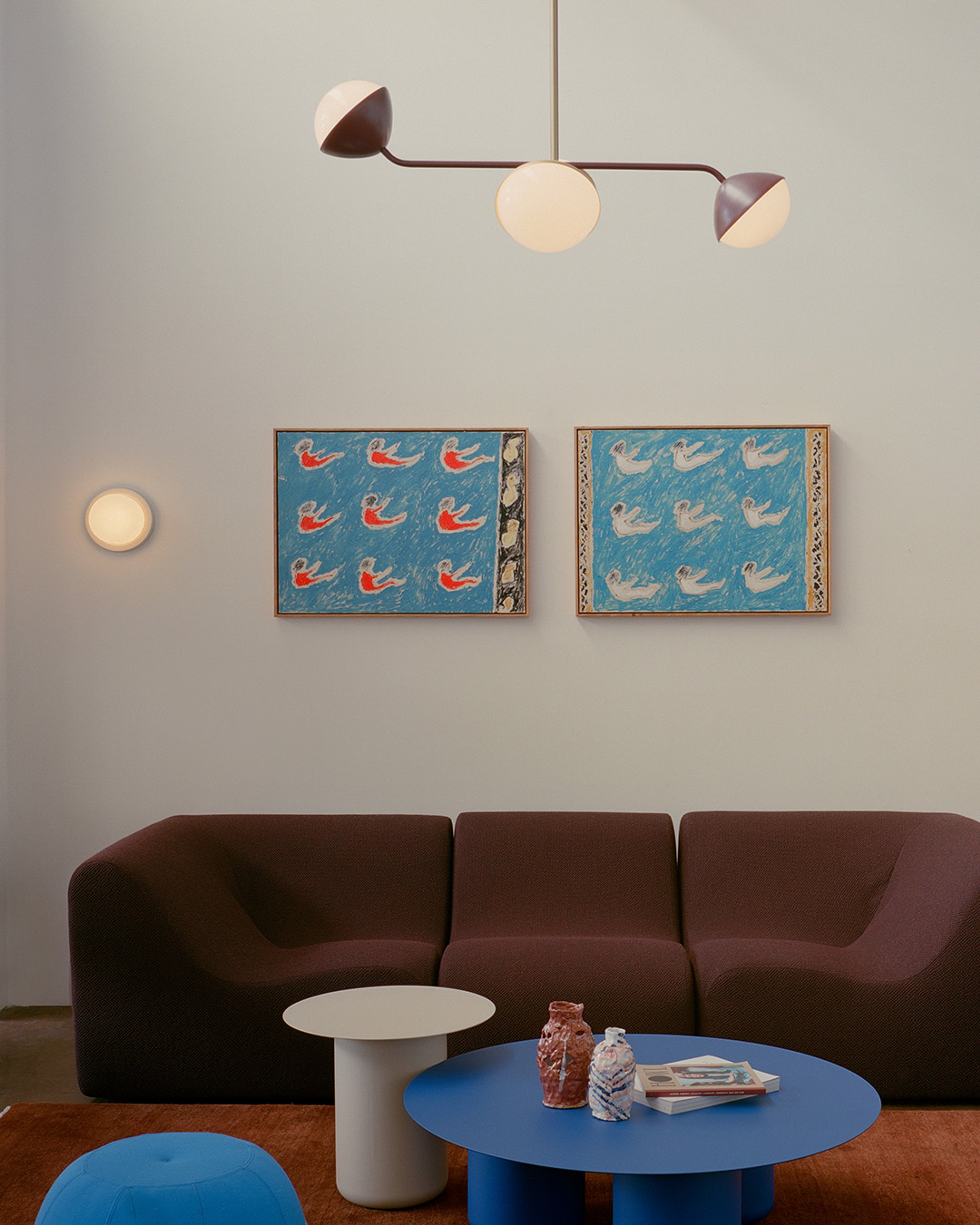 Jolly double rod pendants in the Coco Flip showroom above a burgundy sofa. The room has white walls, artwork and colourful coffee table