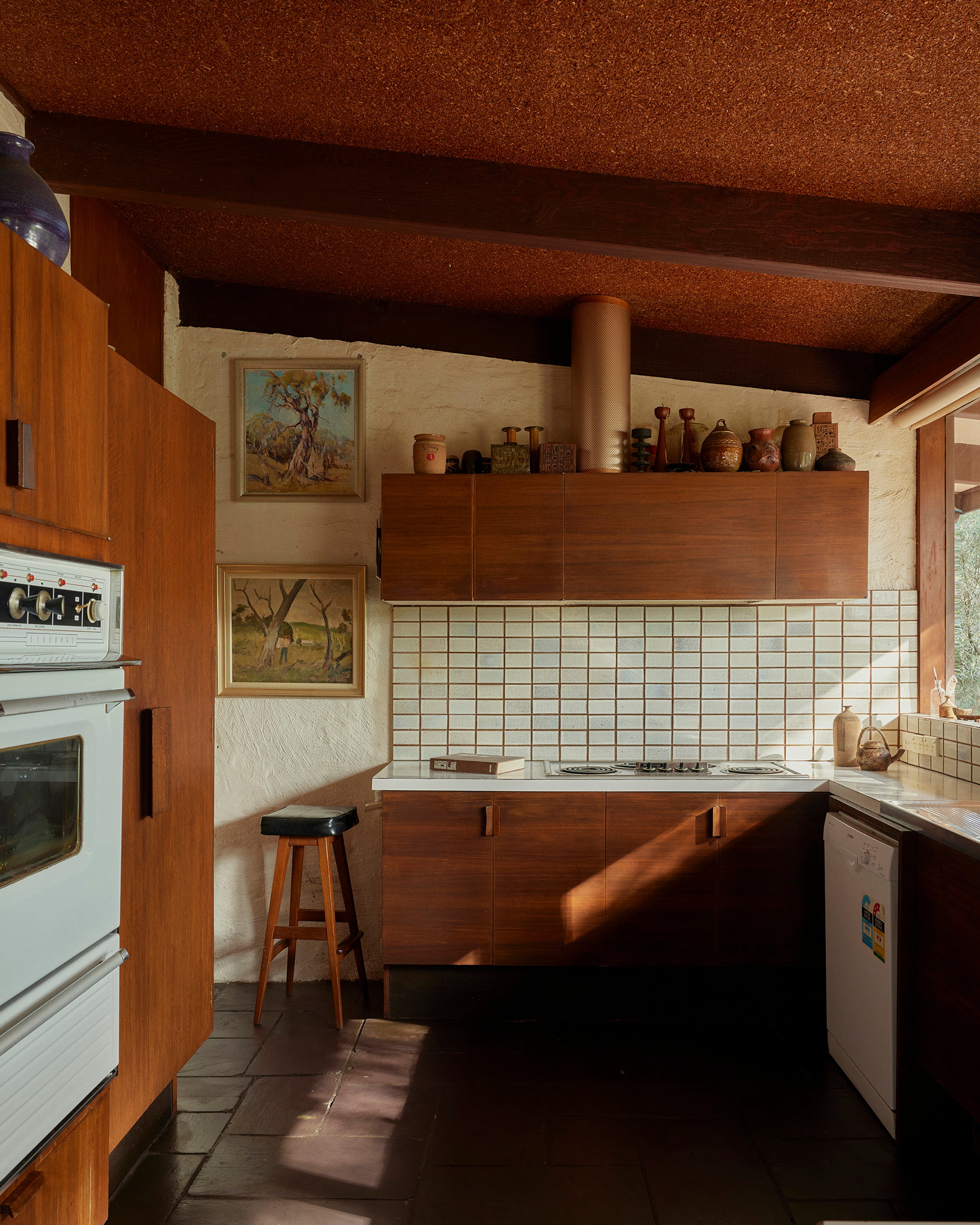 A modernist 70s kitchen with slate tiled floors, timber cabinetry and tiled splash back.