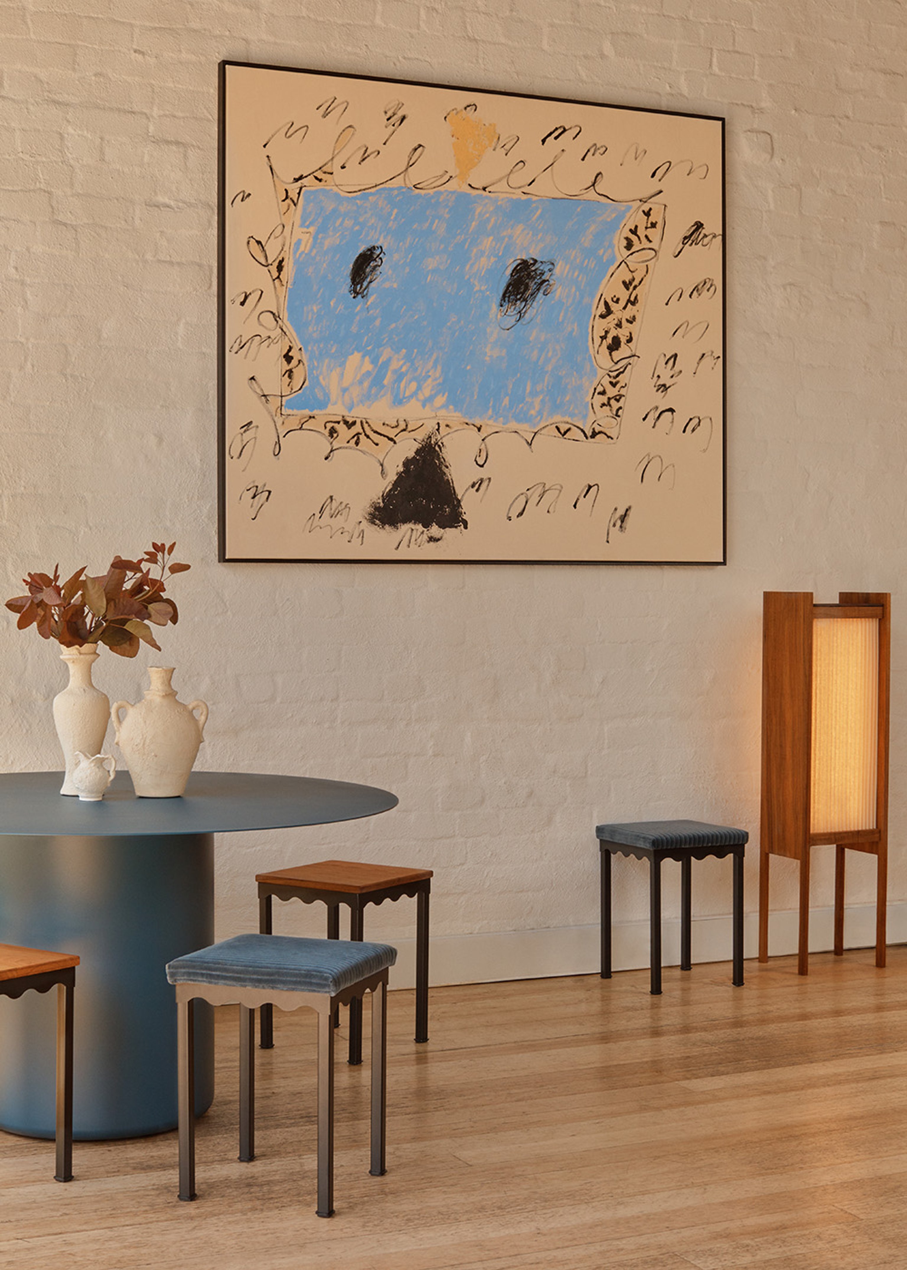 A large painting on a wall in a room with timber floors, a Sequence Round Dining Table (blue) and Bellini Stools.