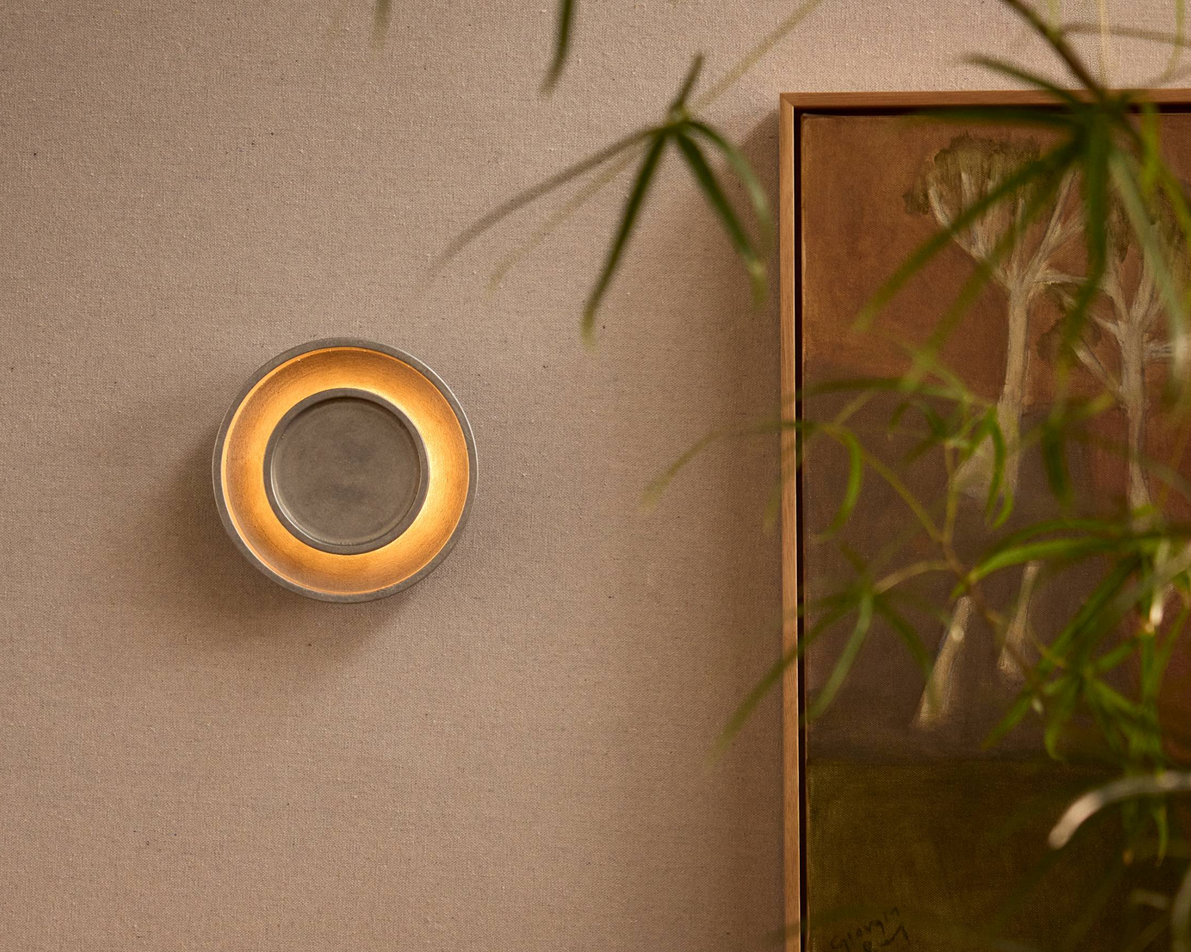 Chorus Wall Light in Aluminium, next to a earth toned painting.