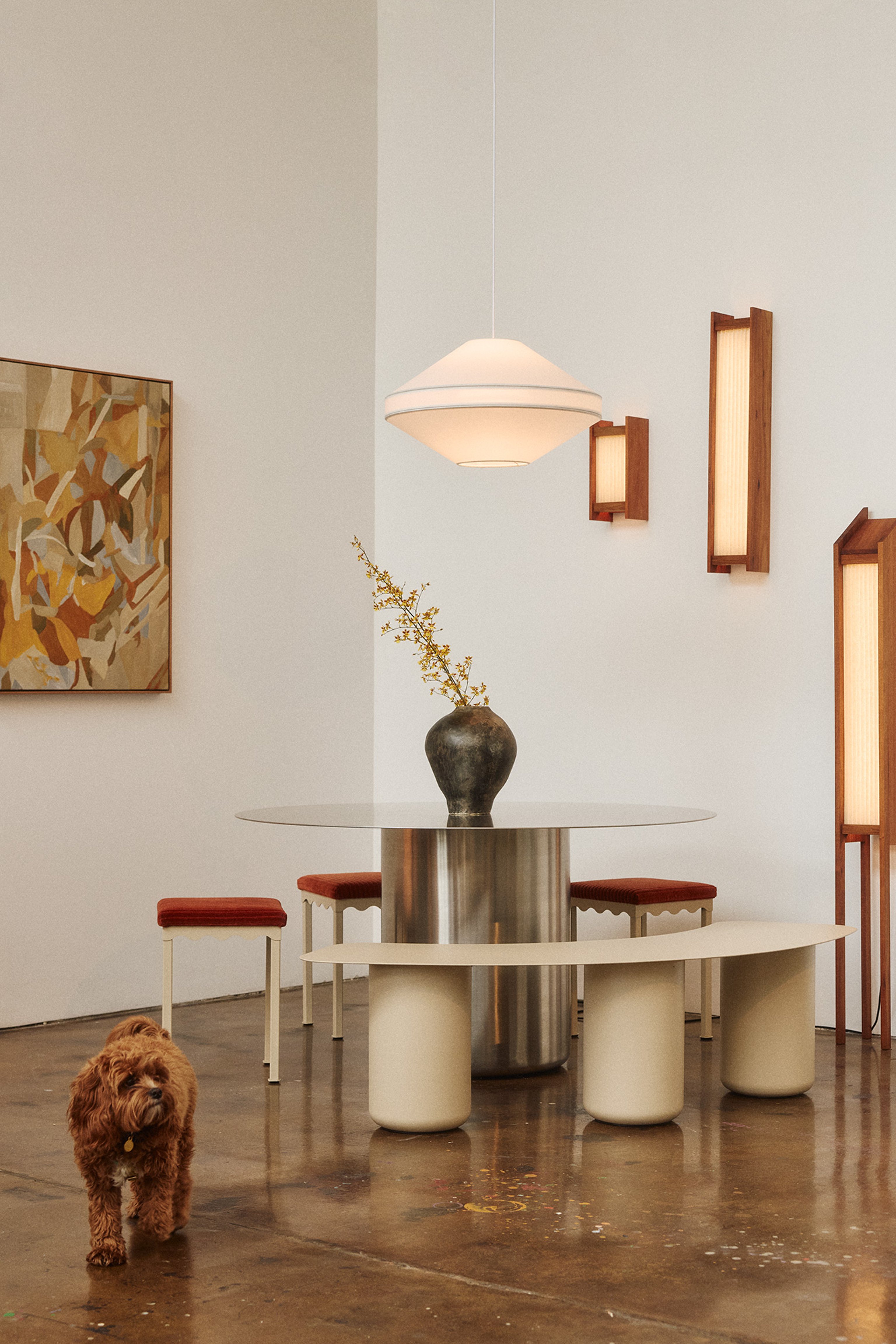 A photograph of the Coco Flip showroom, with a stainless steel dining table, paperbark bench and pendant and wall lighting. A dog in the foreground.