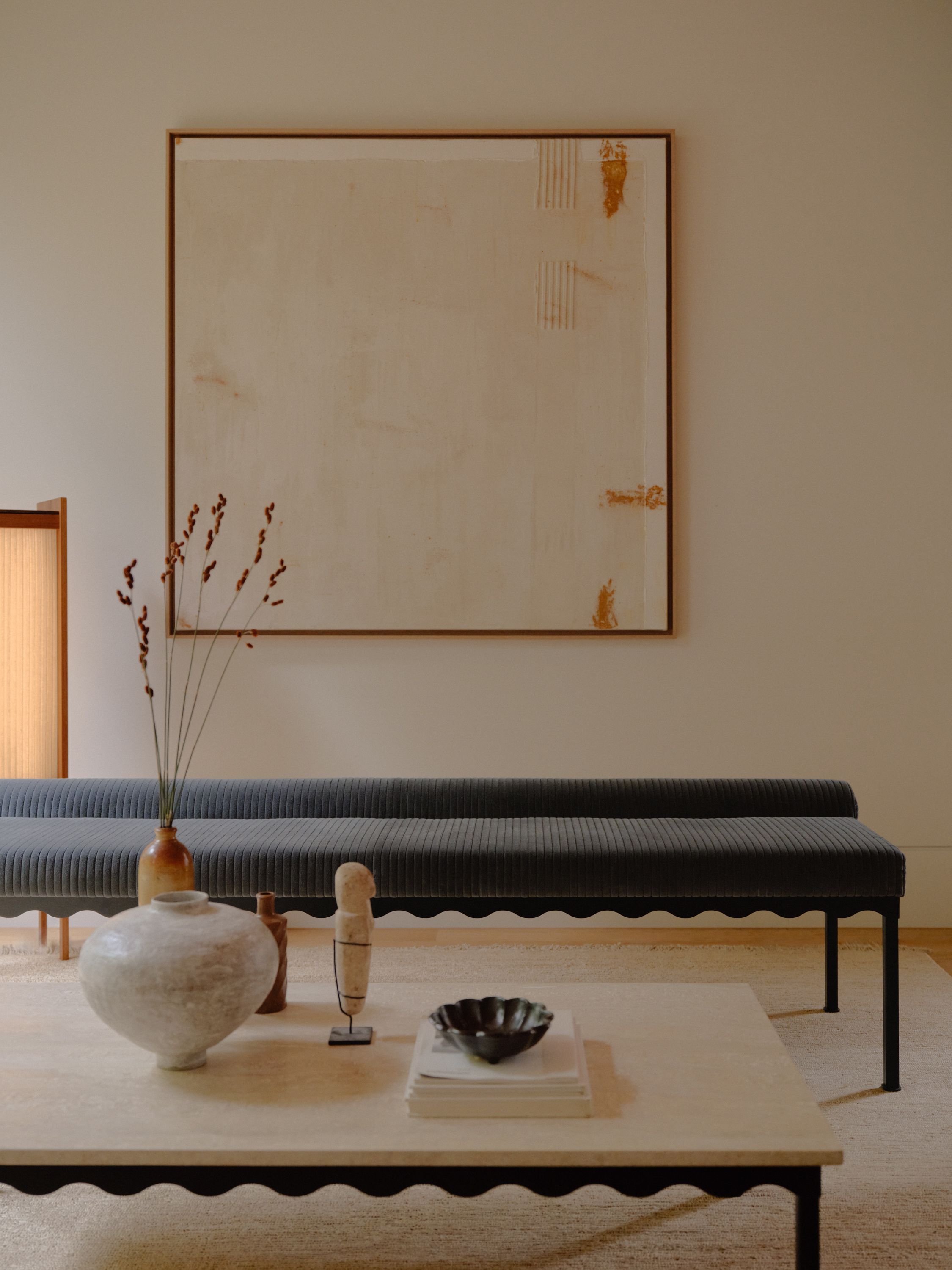 A blue corduroy upholstered Bellini bench seat in a room with a stone Bellini Coffee table. A large neutral artwork is hung on the wall with some warm lighting from a timber floorlamp