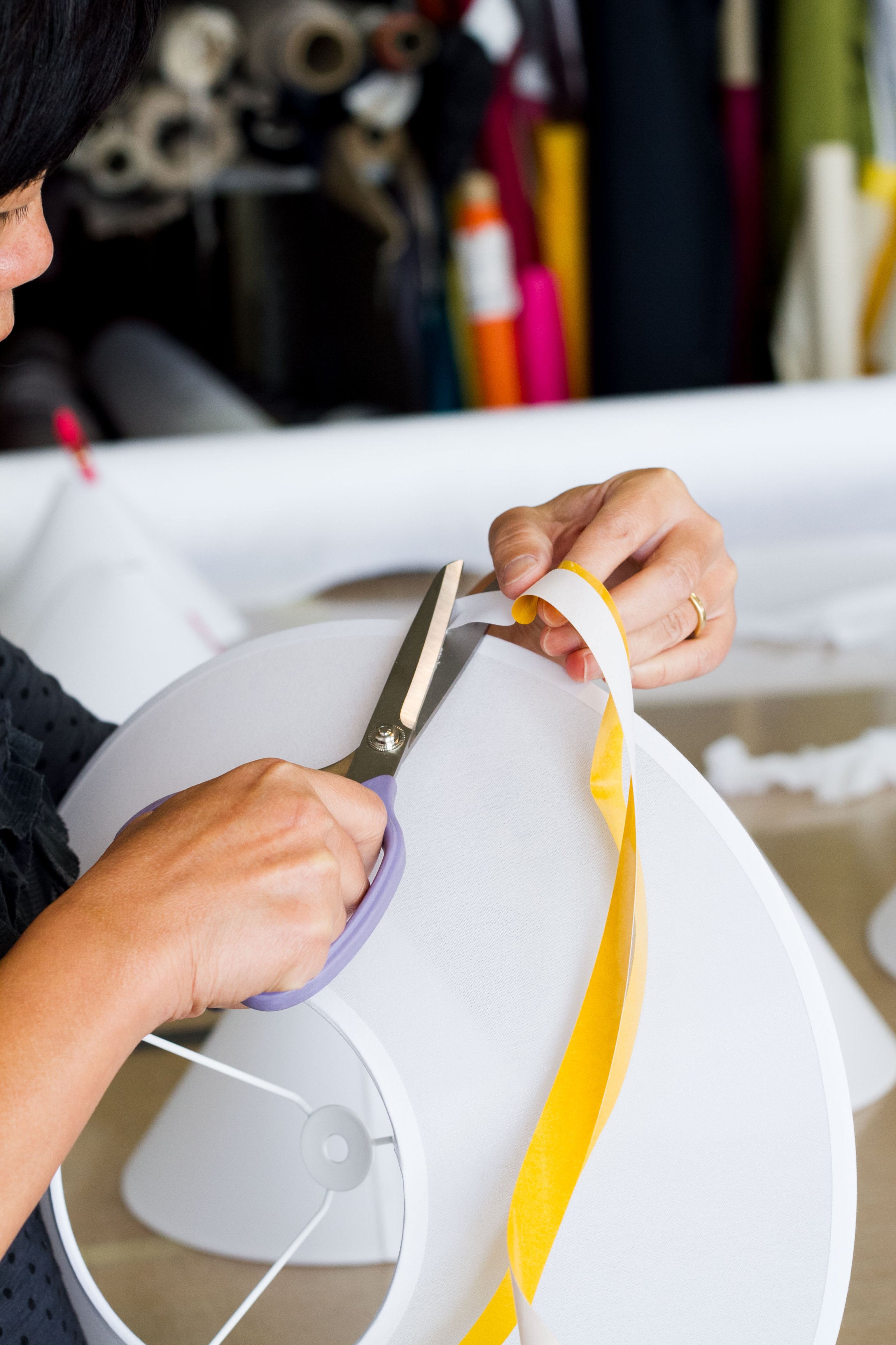 A woman cutting tape with scissors and affixing it to a white fabric shade
