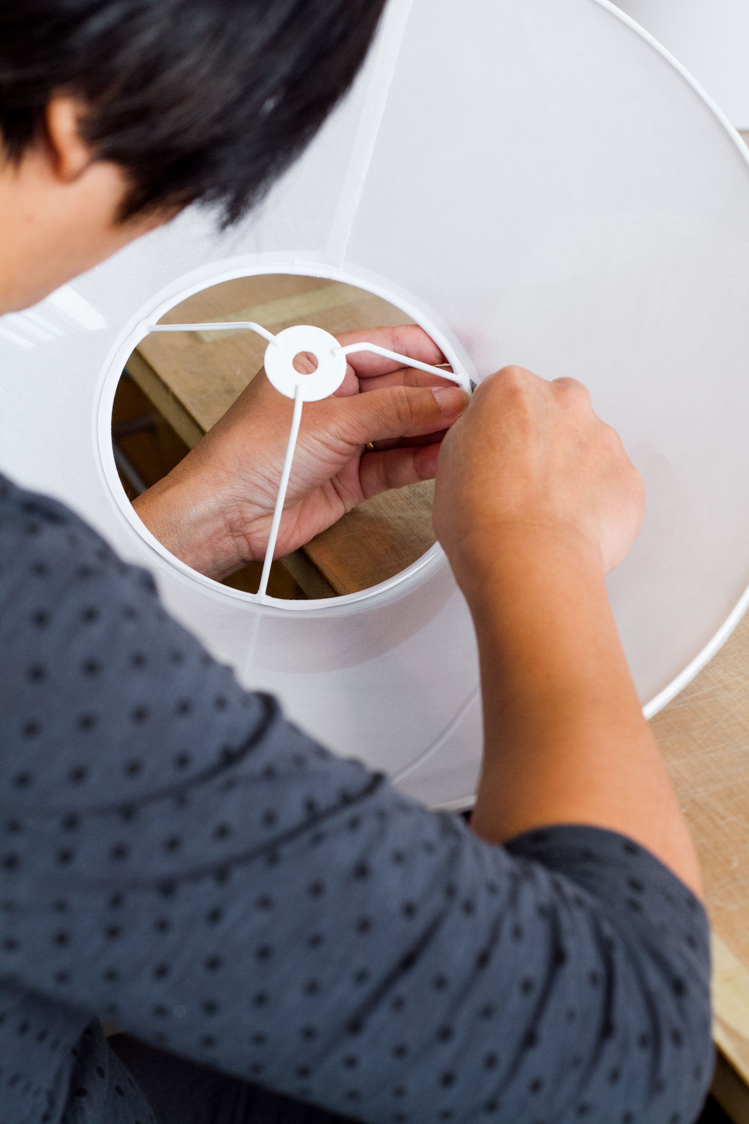 A woman carefully constructs a white fabric shade around a wire frame