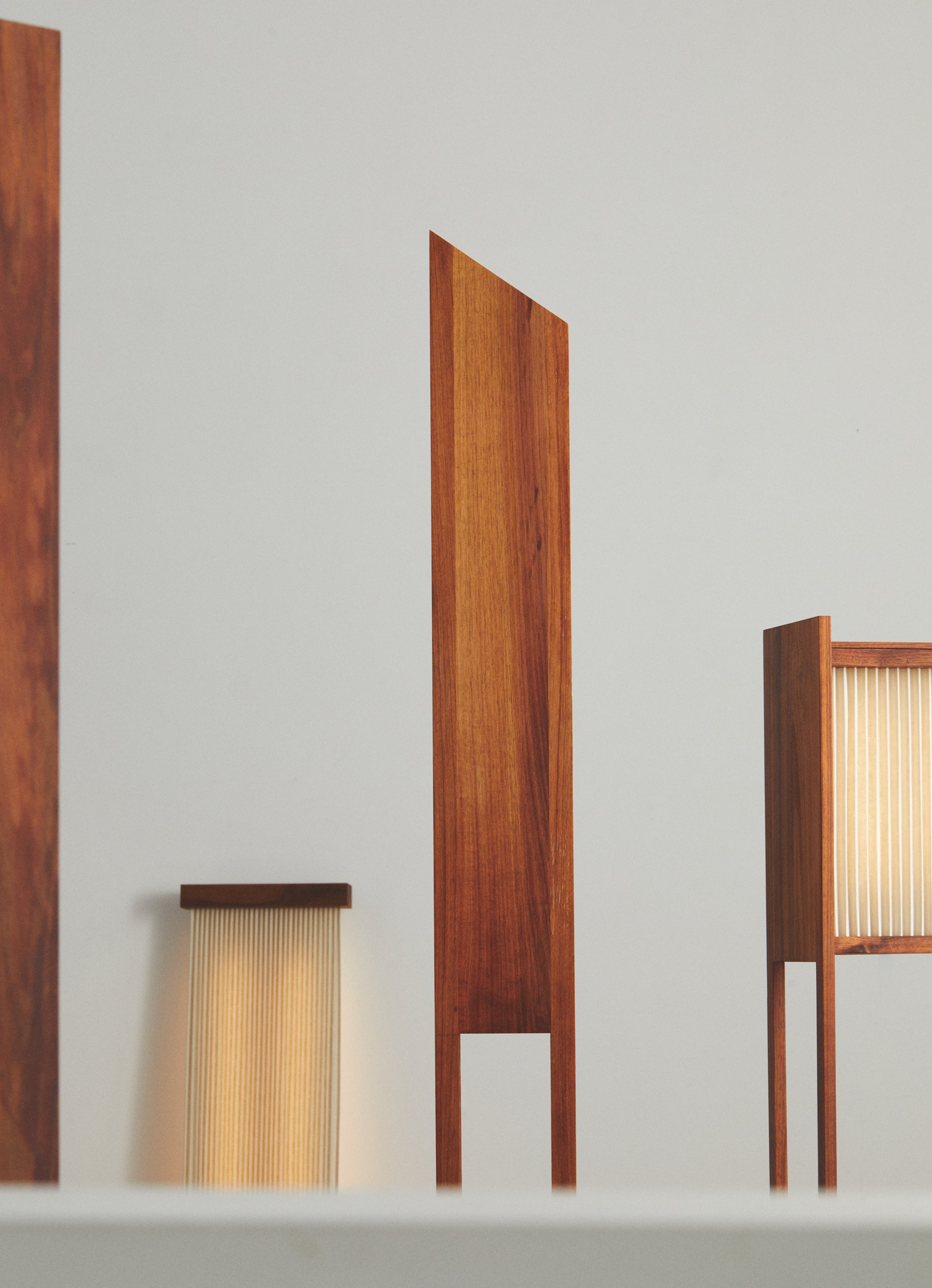 A collection of contemporary pleated linen floor lamps with timber base and warm glow, standing upright against a plain background.