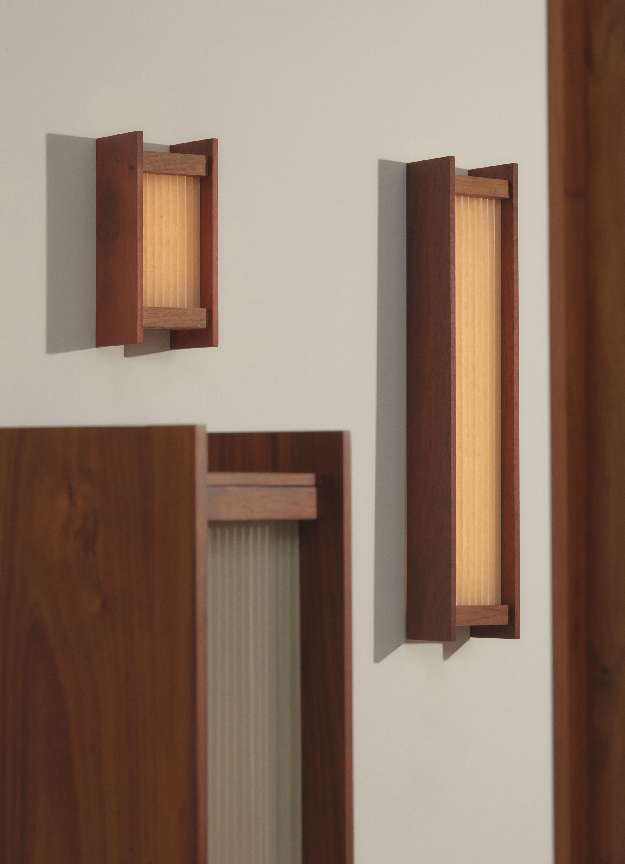 A collection of contemporary pleated linen light sculptures with timber base and warm glow, standing upright against a plain background.