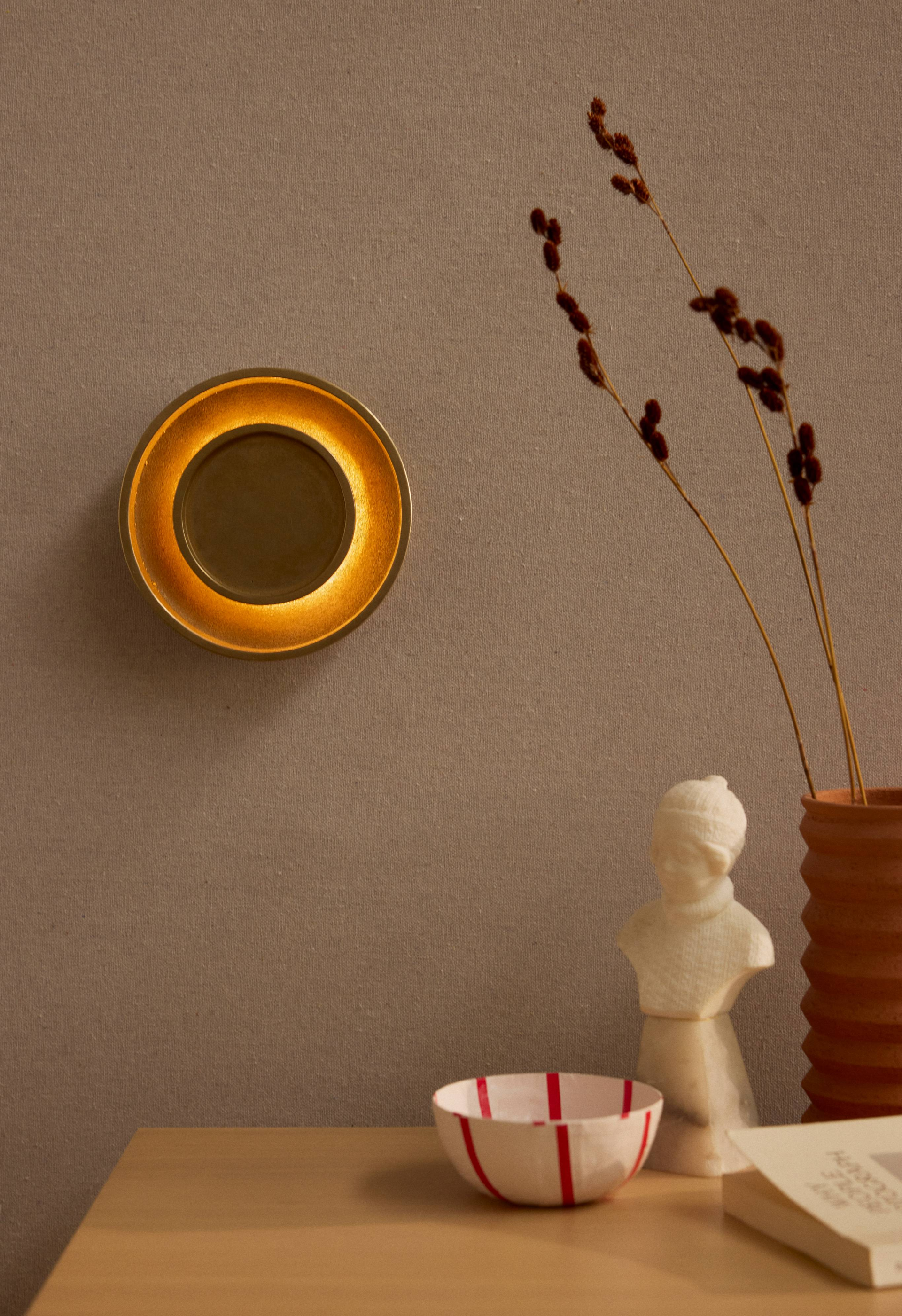 Chorus Wall Light in cast brass behinf a table top of objects