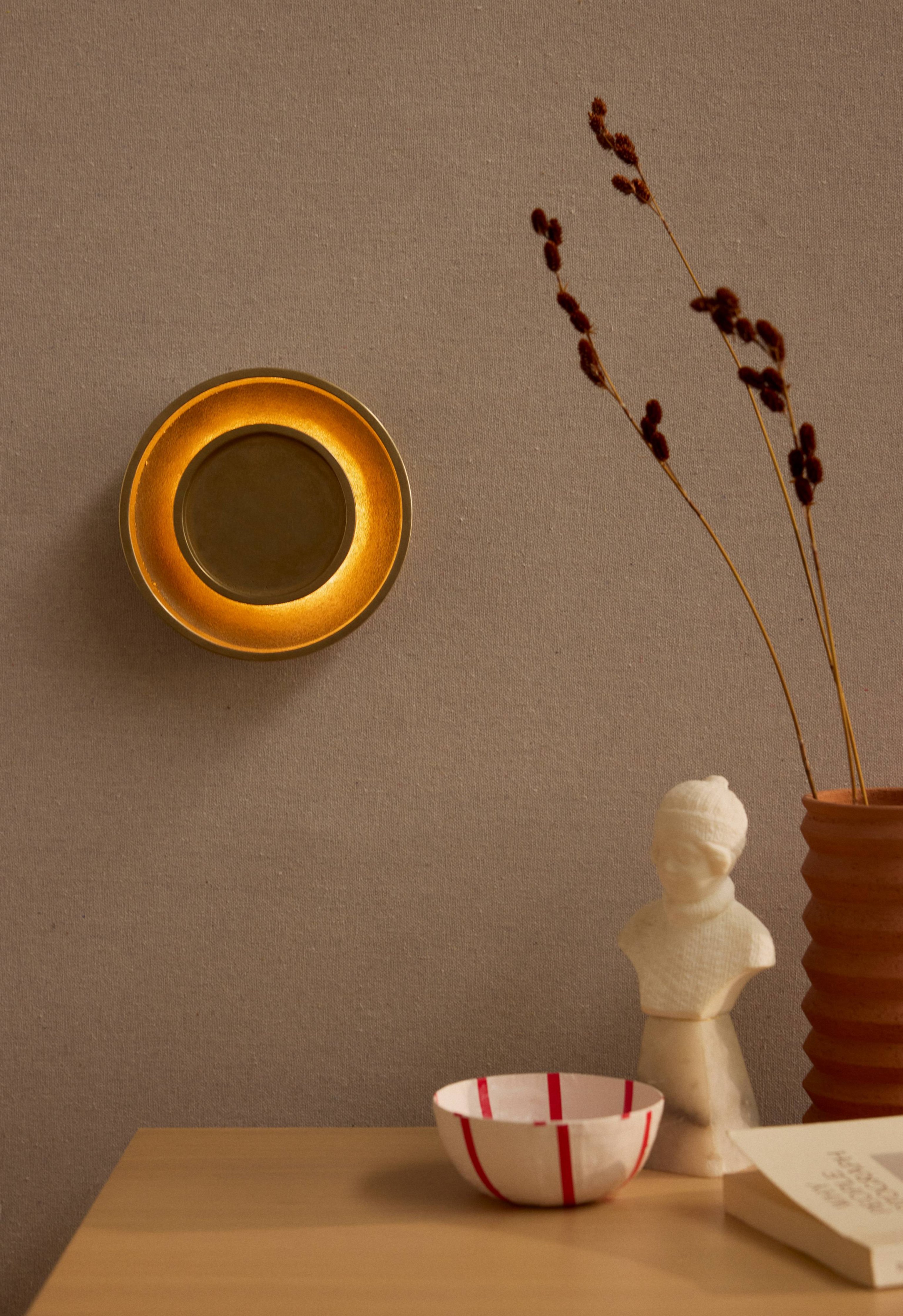 Chorus Wall Light in cast brass behinf a table top of objects