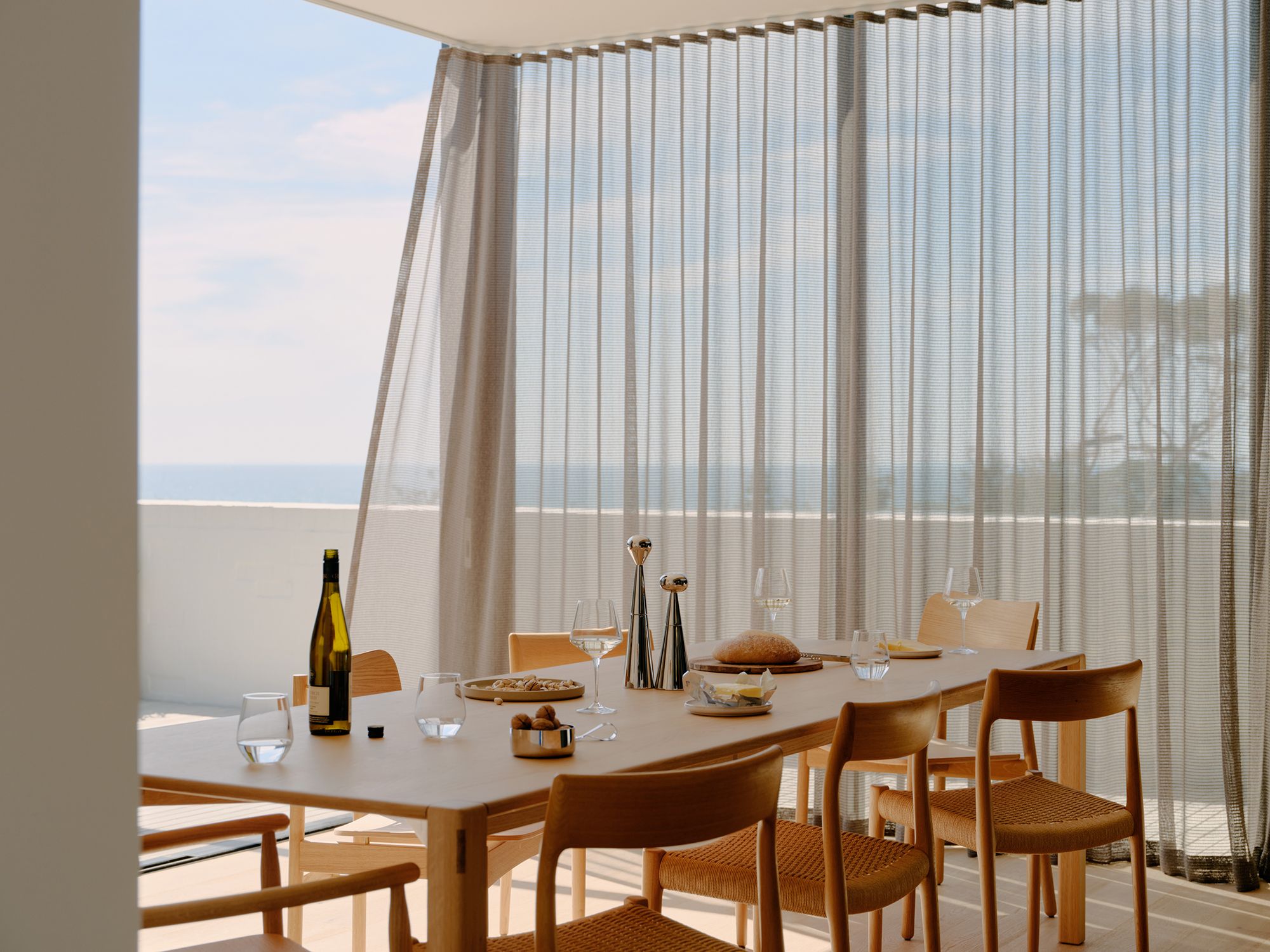 A large dining room with sheer curtains and cloudy blue sky