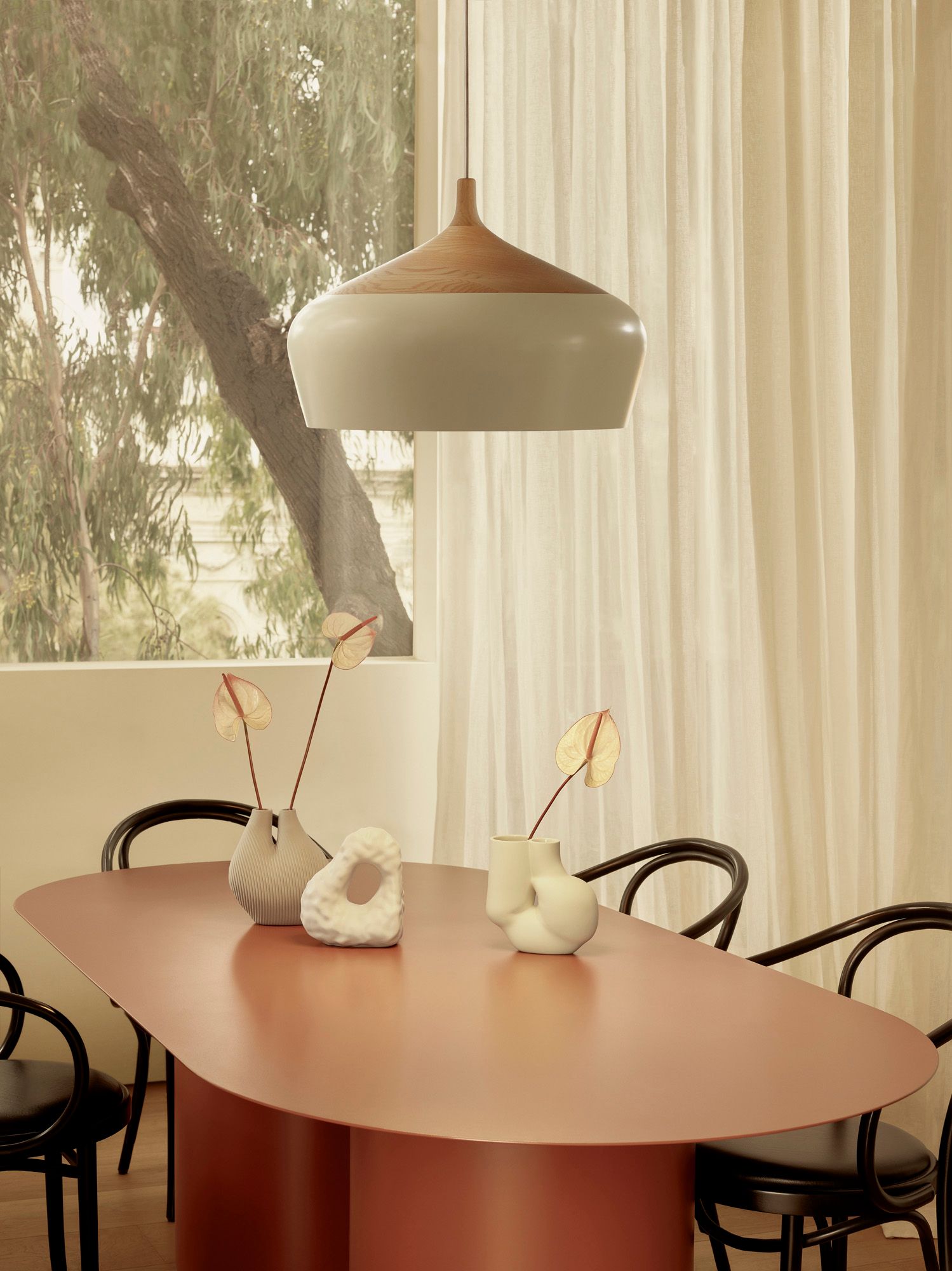 A dining room with a red steel oval dining table and coco pendant