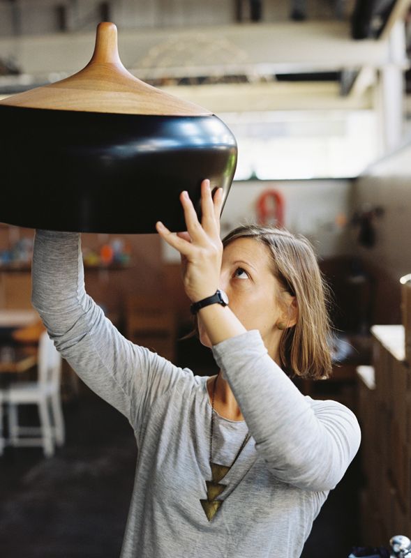 A younger Kate Stokes holds up and inspects a Coco Pendant in an early studio in 2010