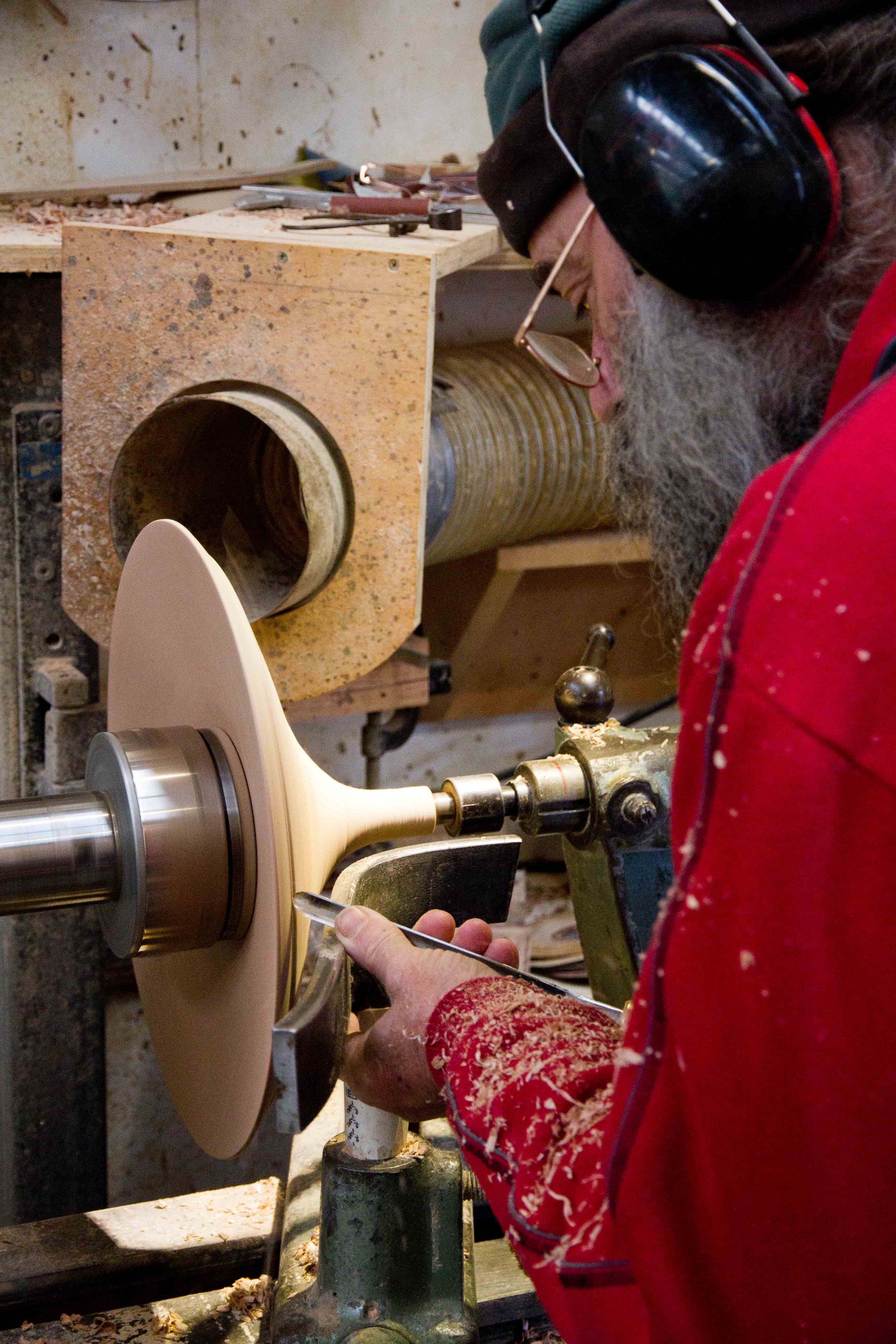 A man uses a tool to turn a laminated piece of timber into the form of a Coco Pendant top.