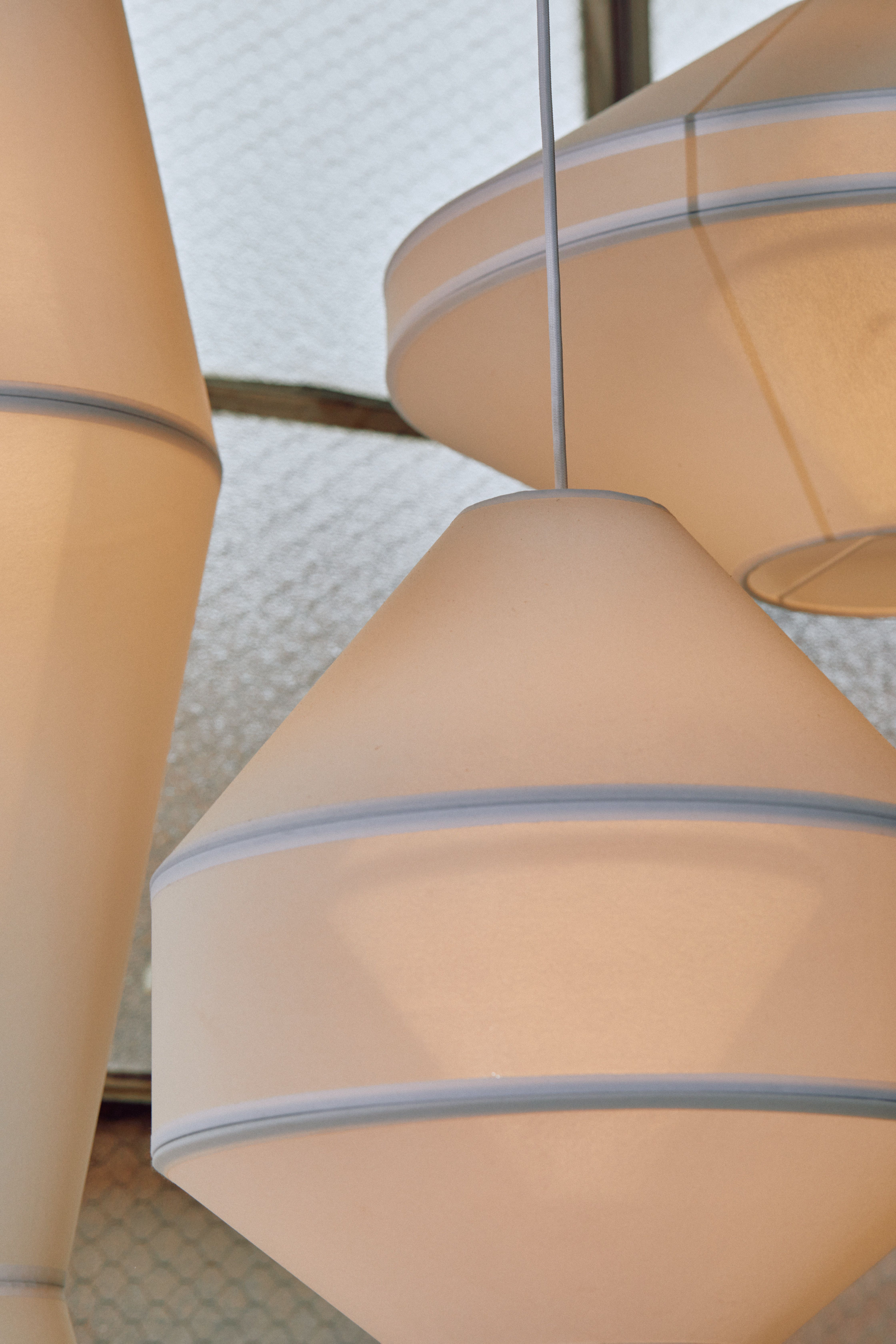 A cluster of Mayu pendant lights, made white mesh fabric. Glass window background