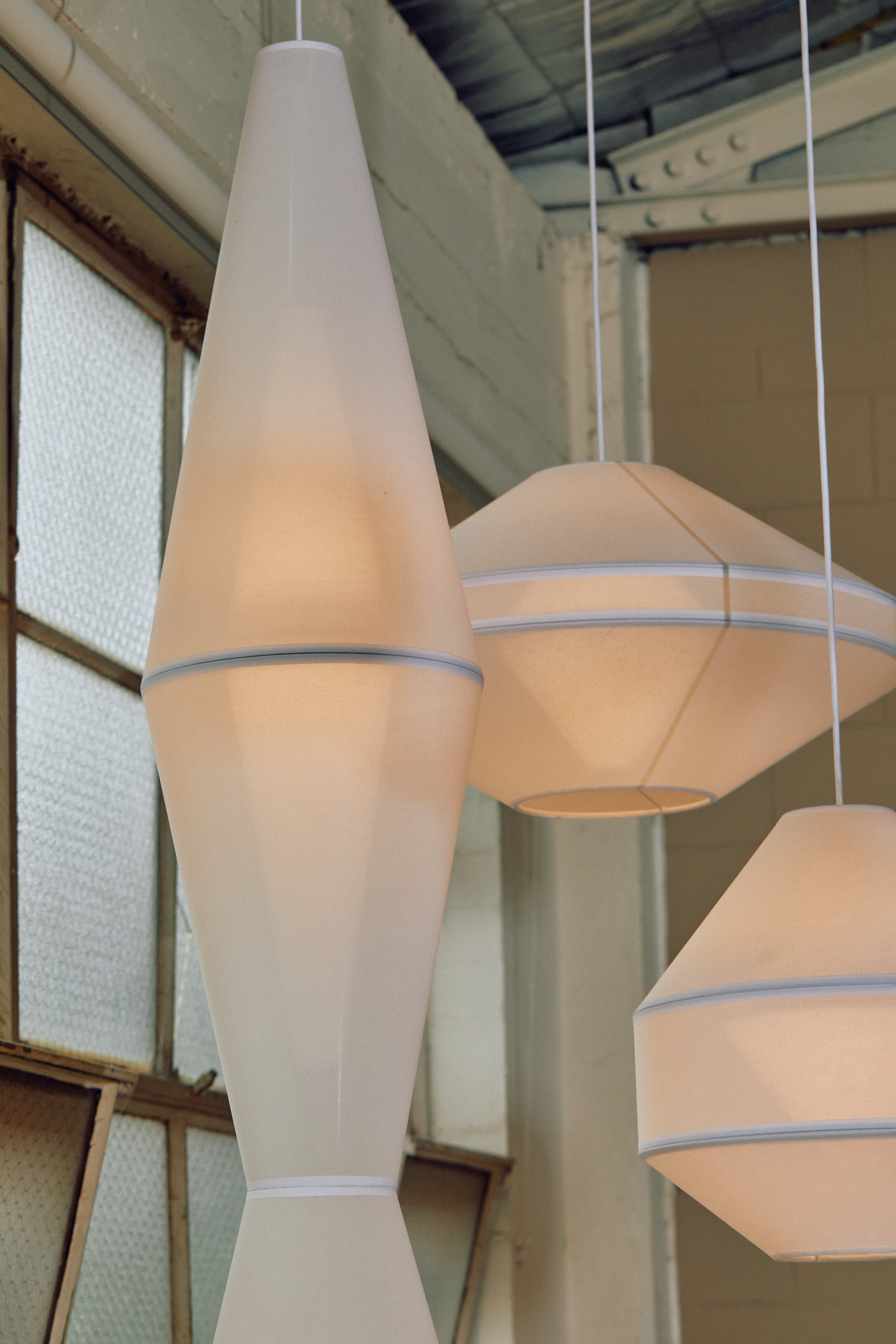 A cluster of Mayu pendant lights, made white mesh fabric. Glass window background