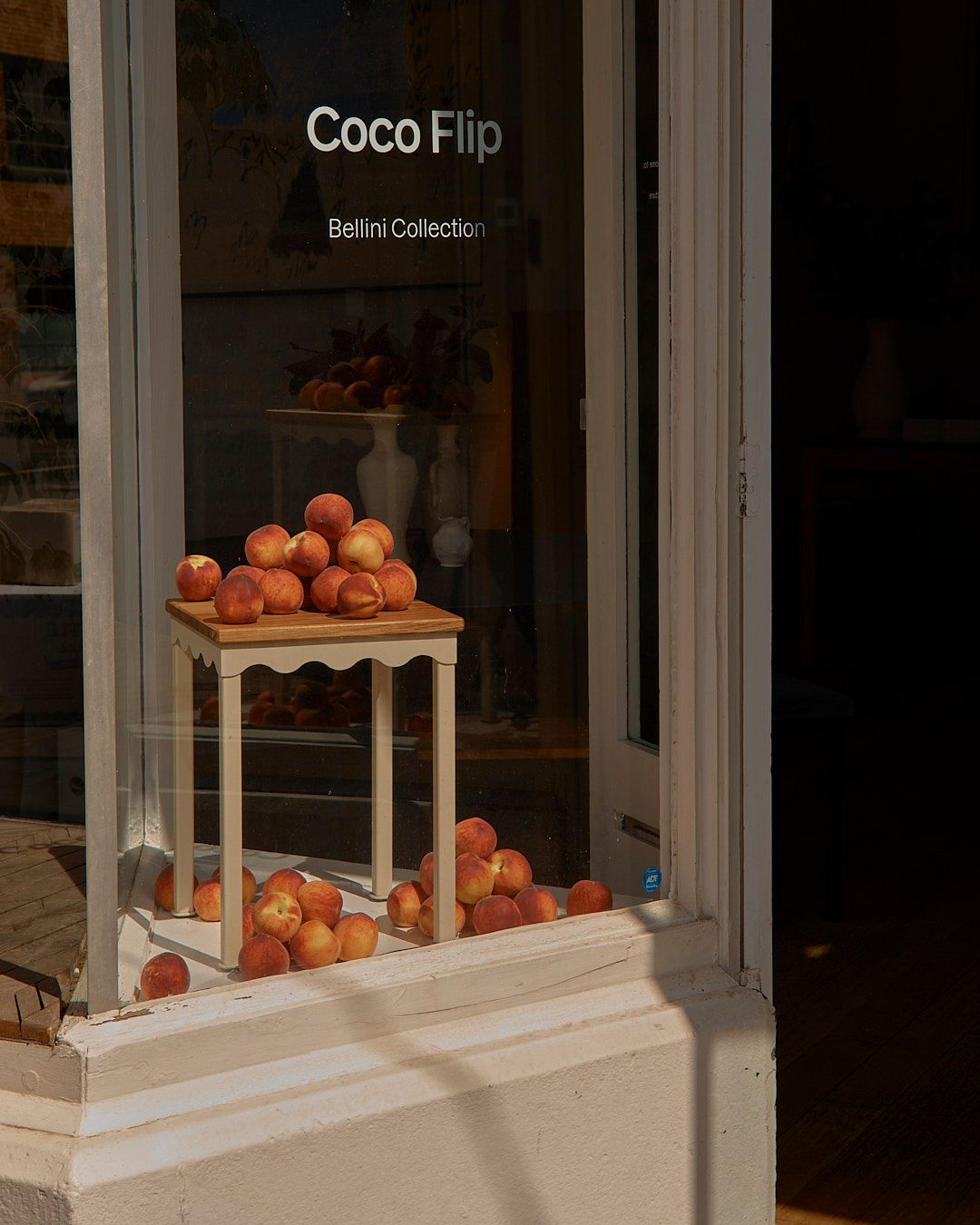 The exterior of a building looking into a window with a Bellini stool stacked with fresh peaches.