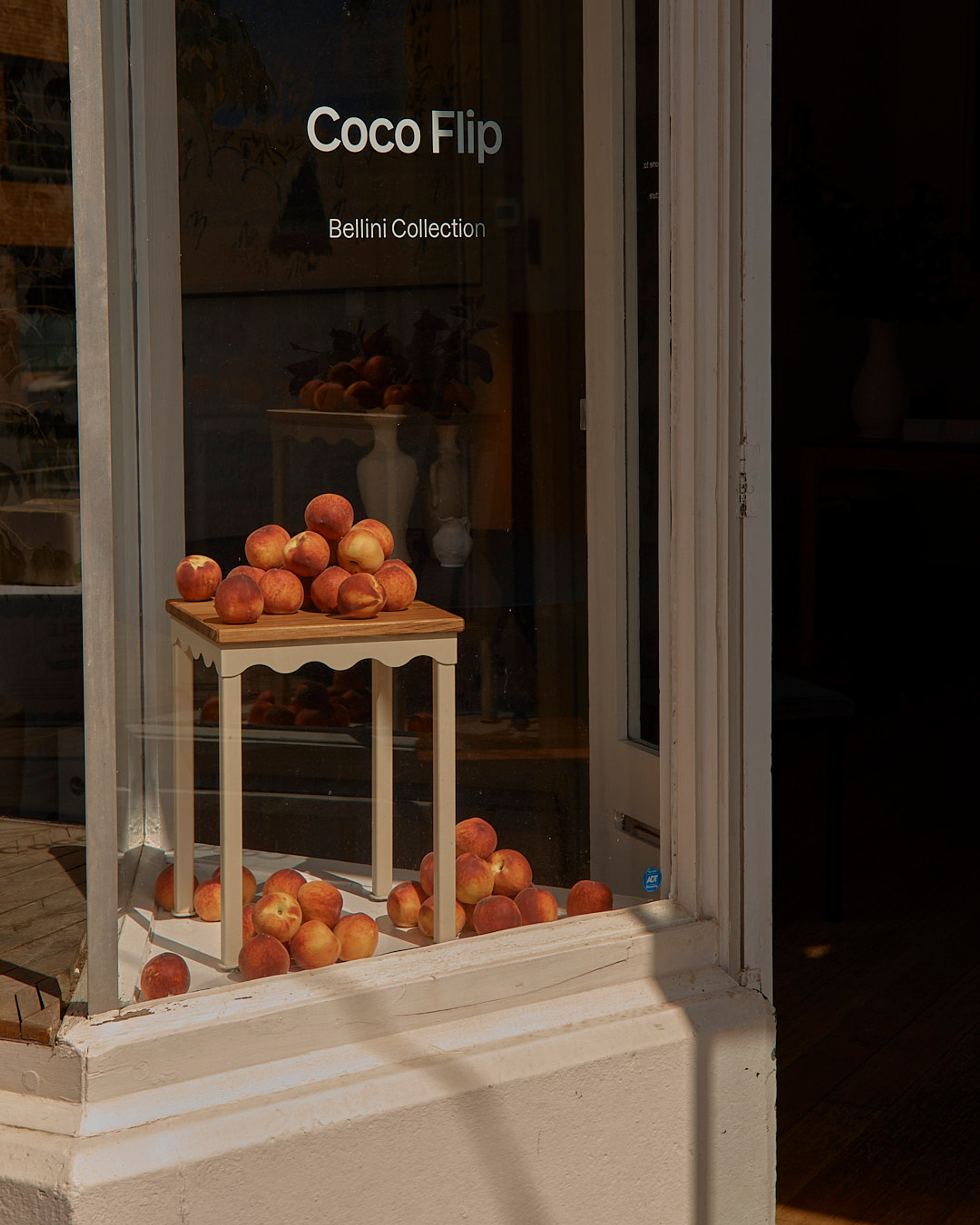 The exterior of a building looking into a window with a Bellini stool stacked with fresh peaches.