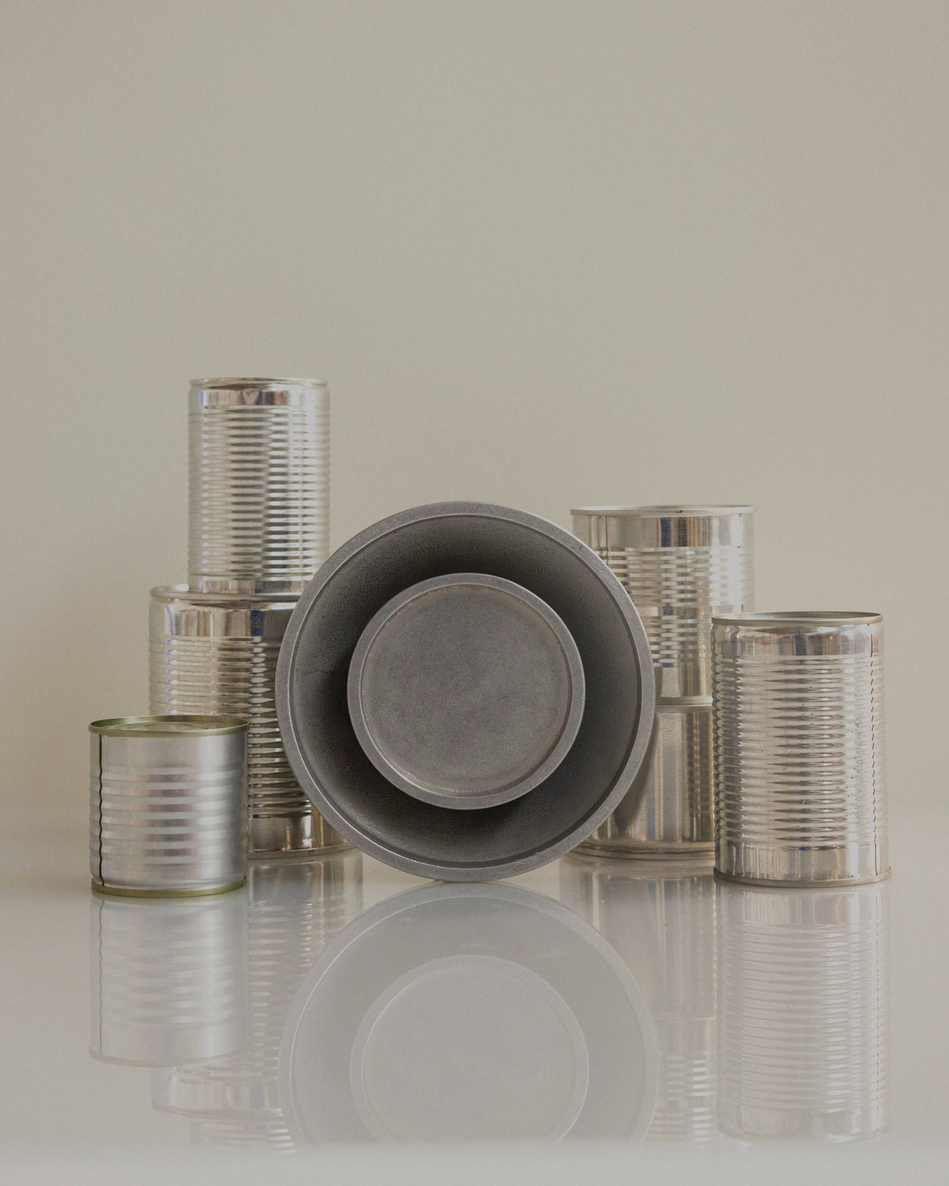 Chorus Wall Light in Aluminium resting against a collection of silver cans.