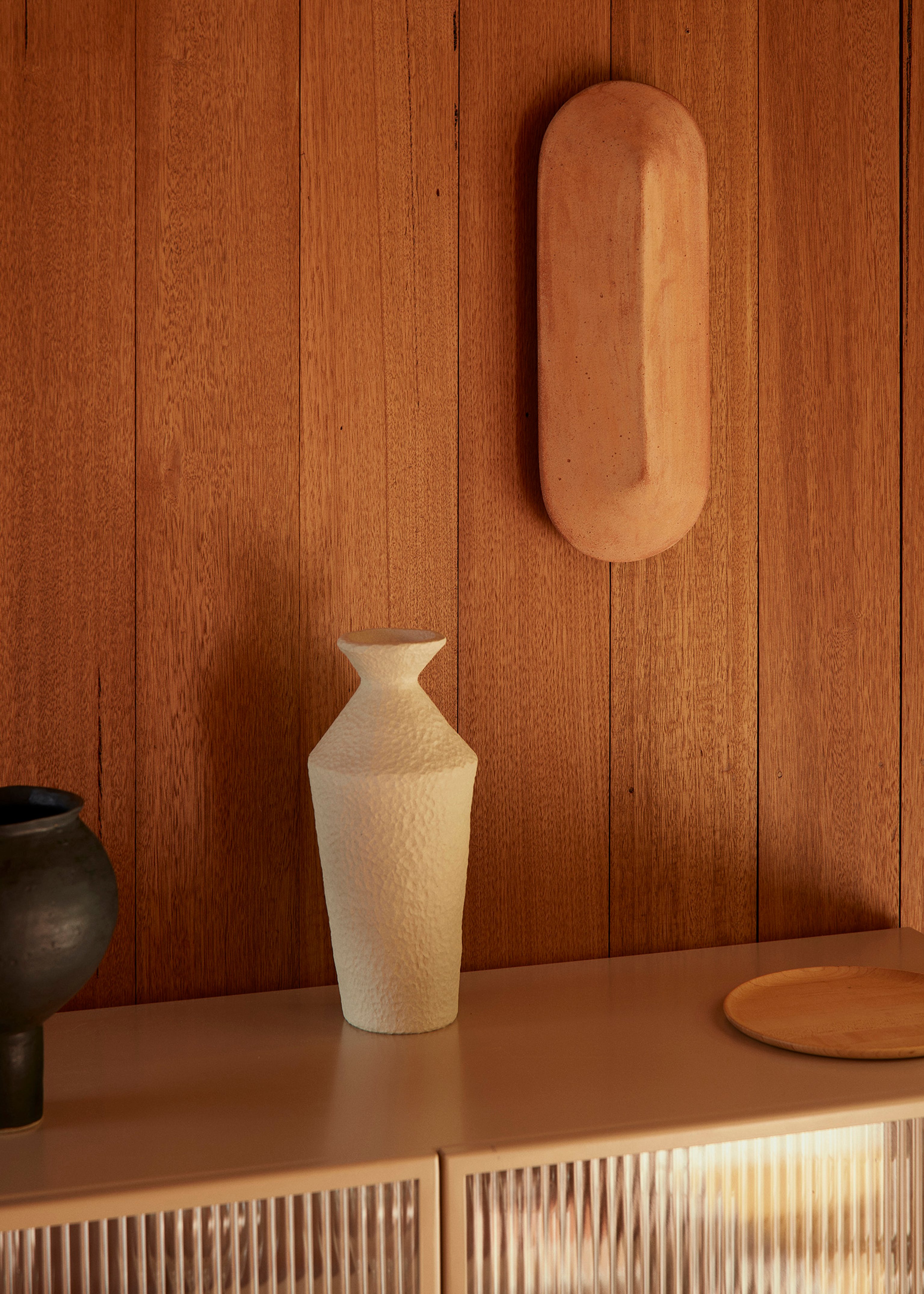 A terracotta pinch wall light mounted on a timber lined wall.