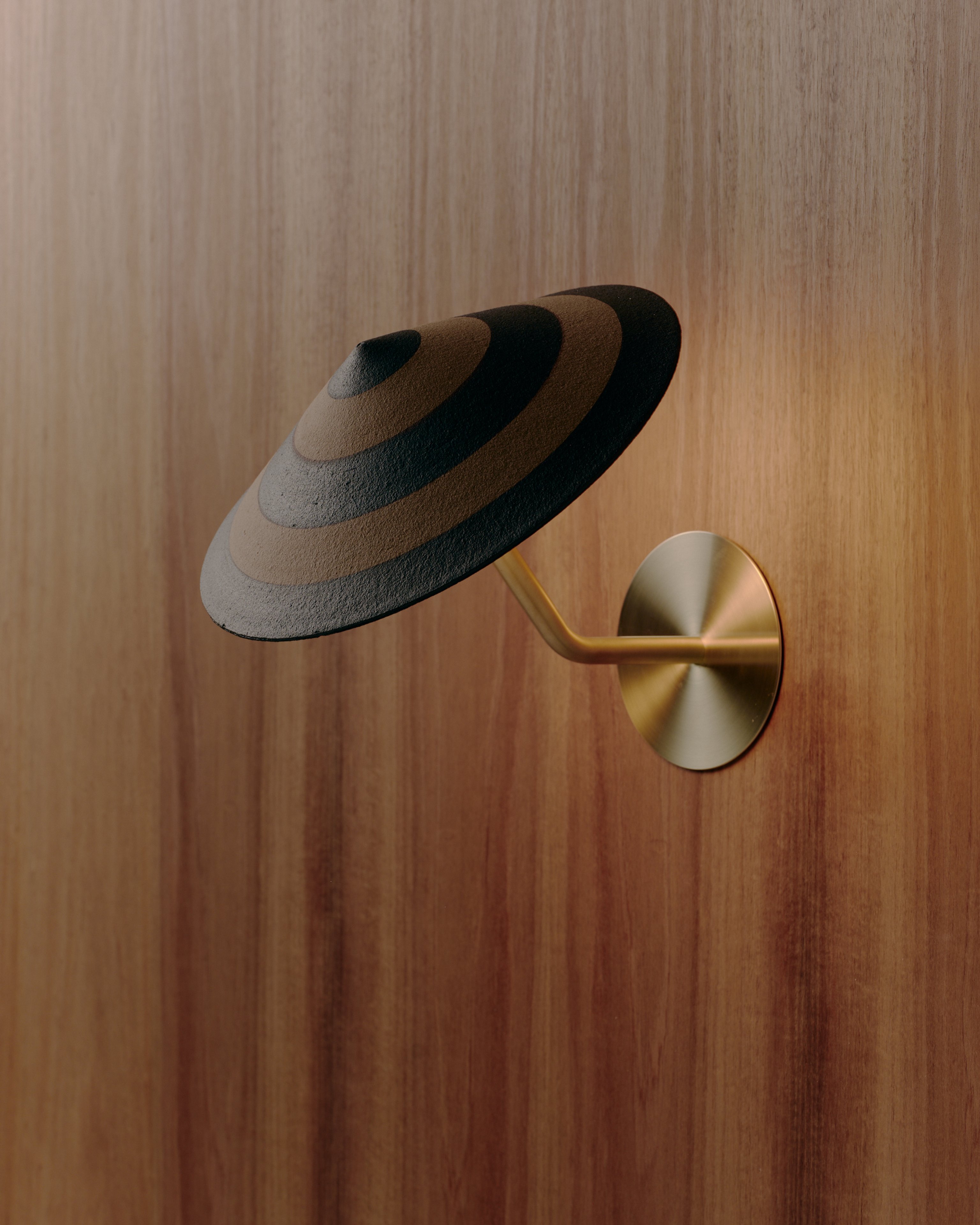 A striped ceramic cone wall light mounted on an angled brass bracket to a timber wall.
