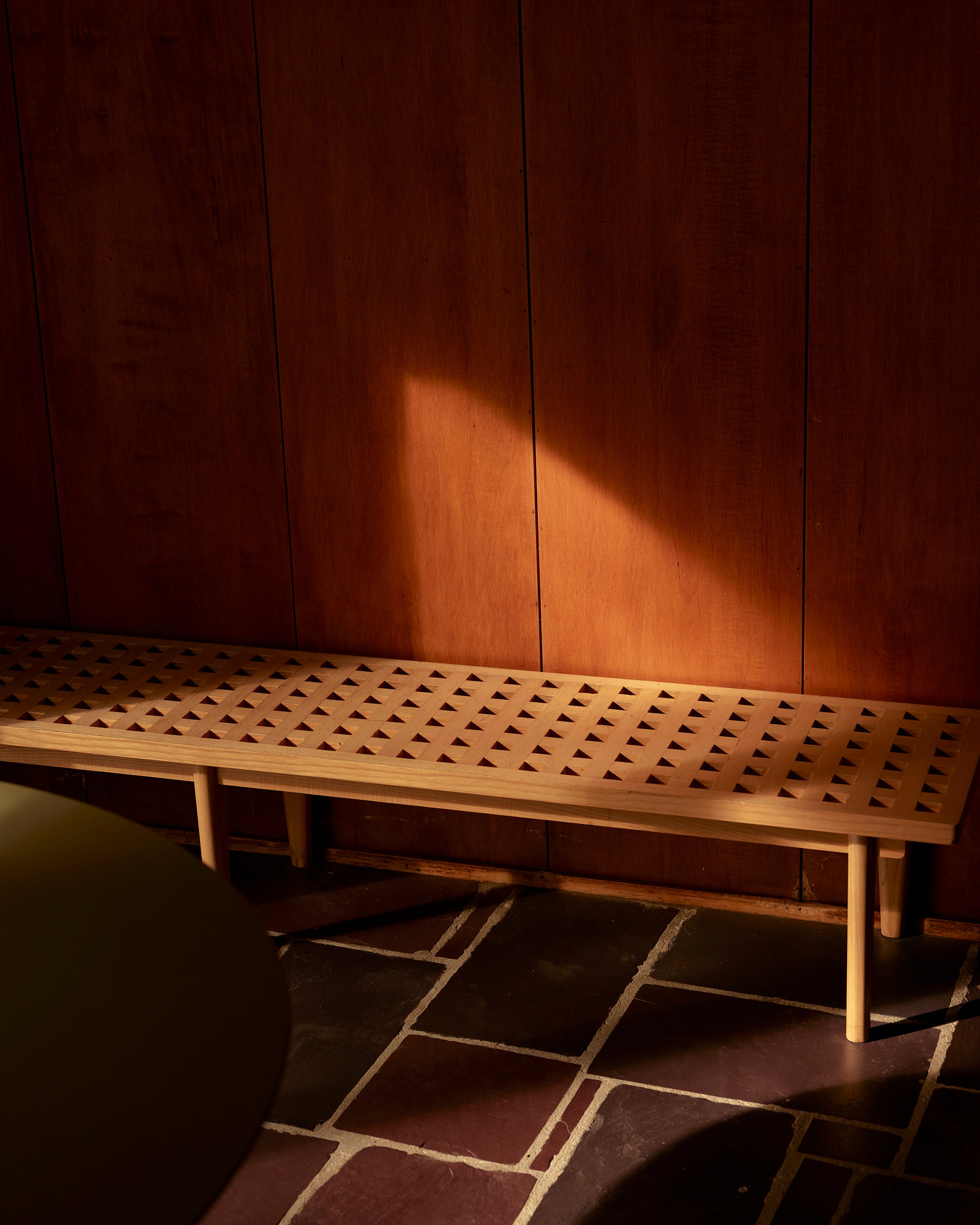 Warm light falls on a timber bench seat and timber lined wall sitting atop slate flooring