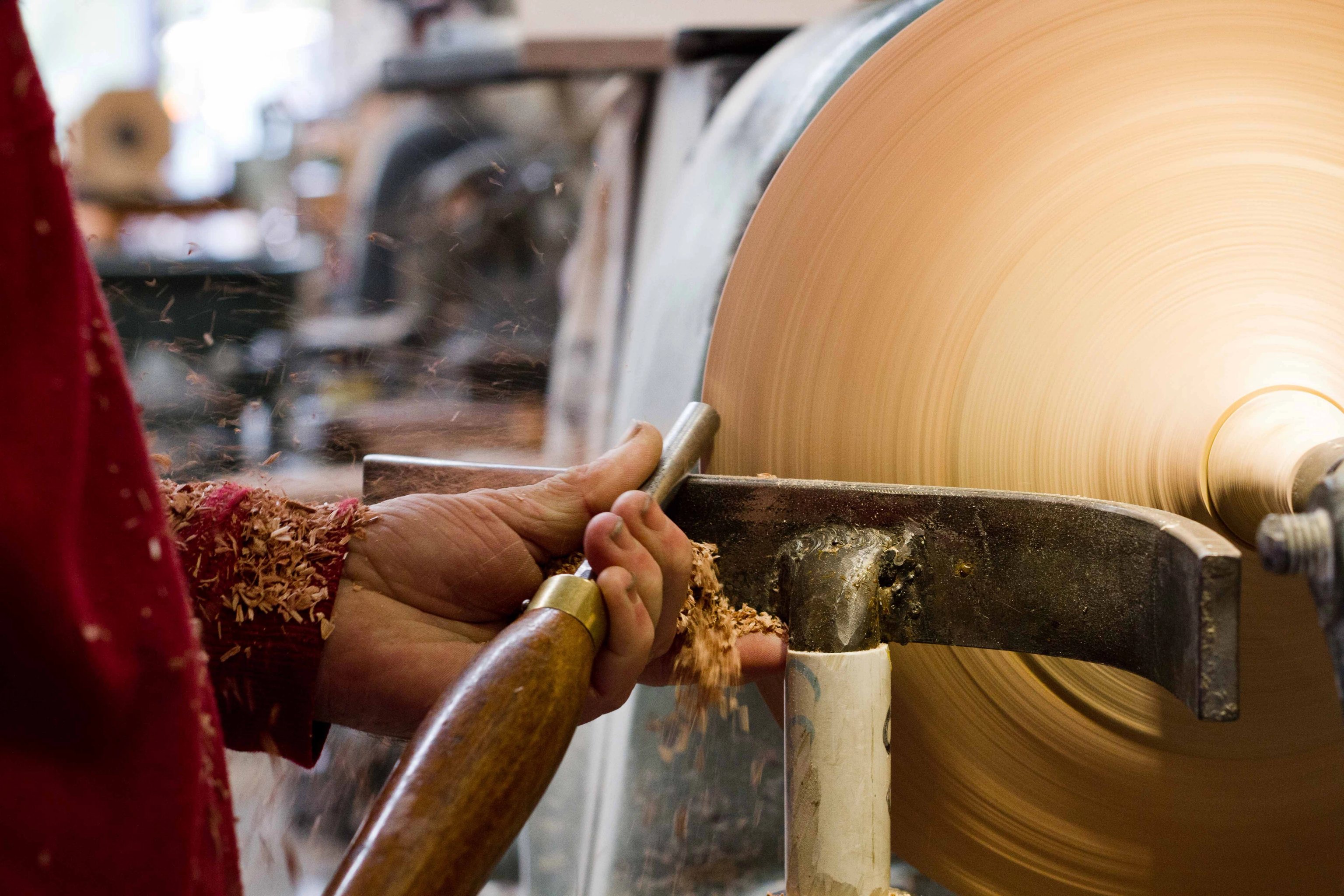 Hands are turning a timber Coco Pendant top using a tool, a metal guide, and a lathe.