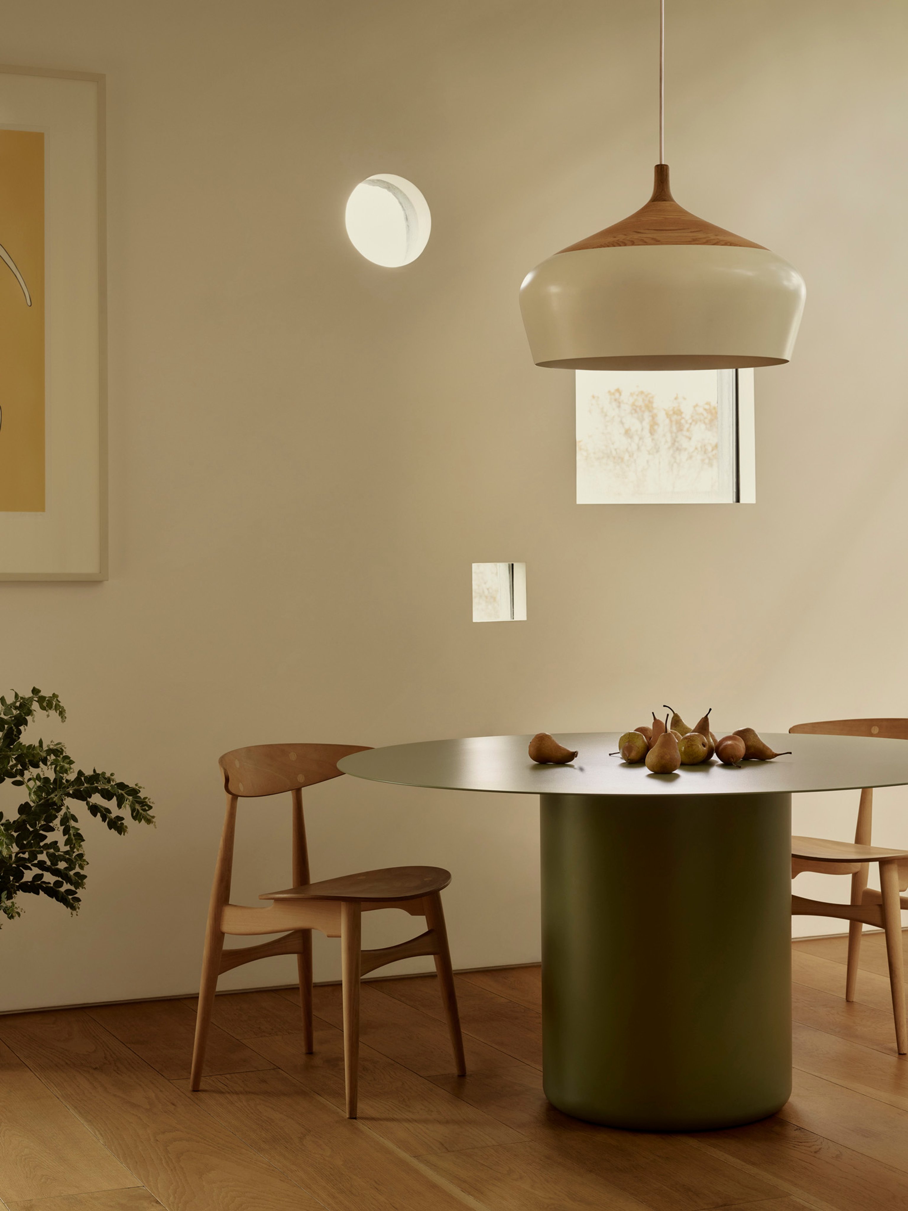 A dining room with a green round dining table and coco pendant