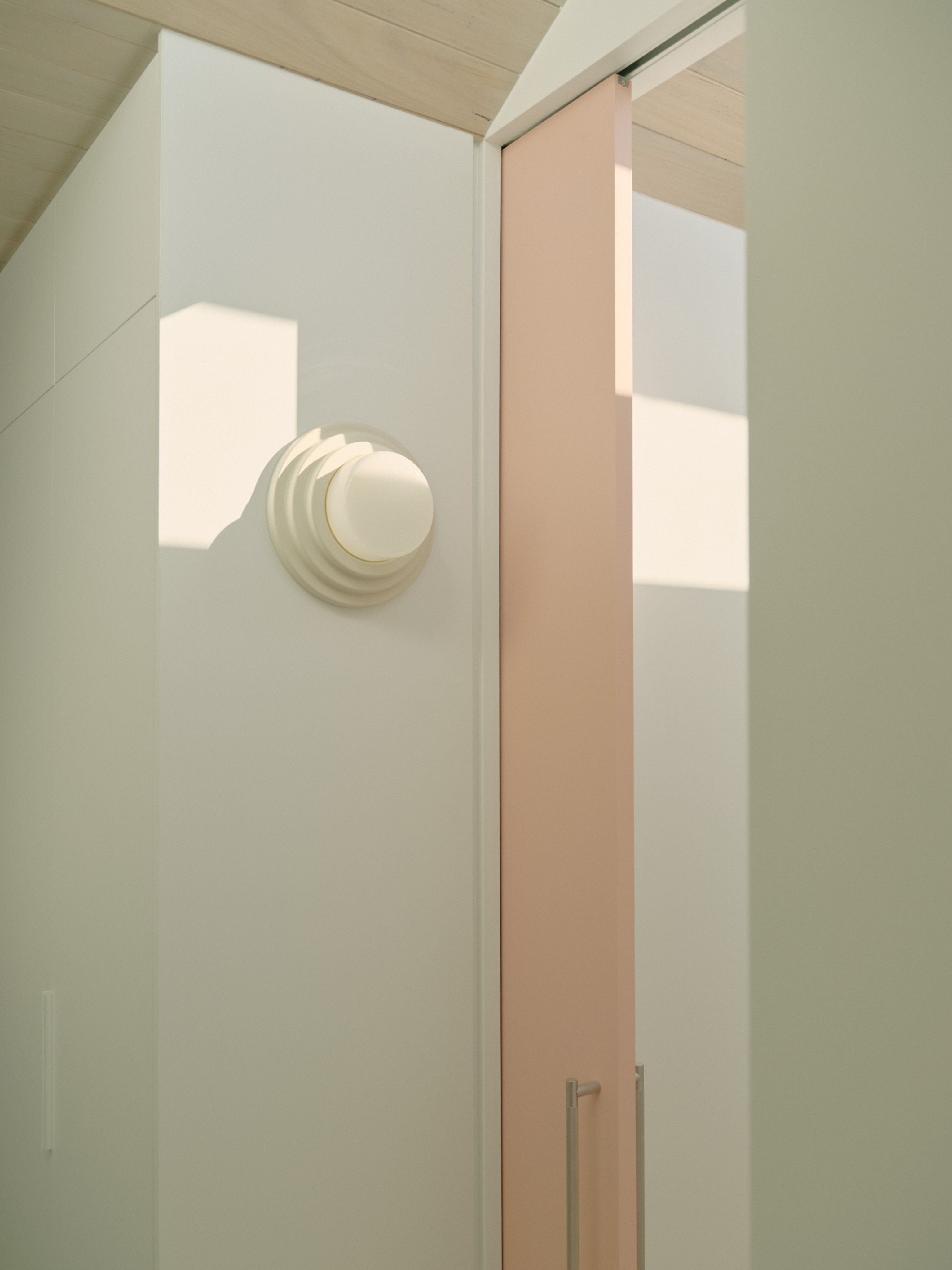 A tiered slip-cast ceramic wall light with a handblown glass diffuser mounted white wall with a pink sliding door.