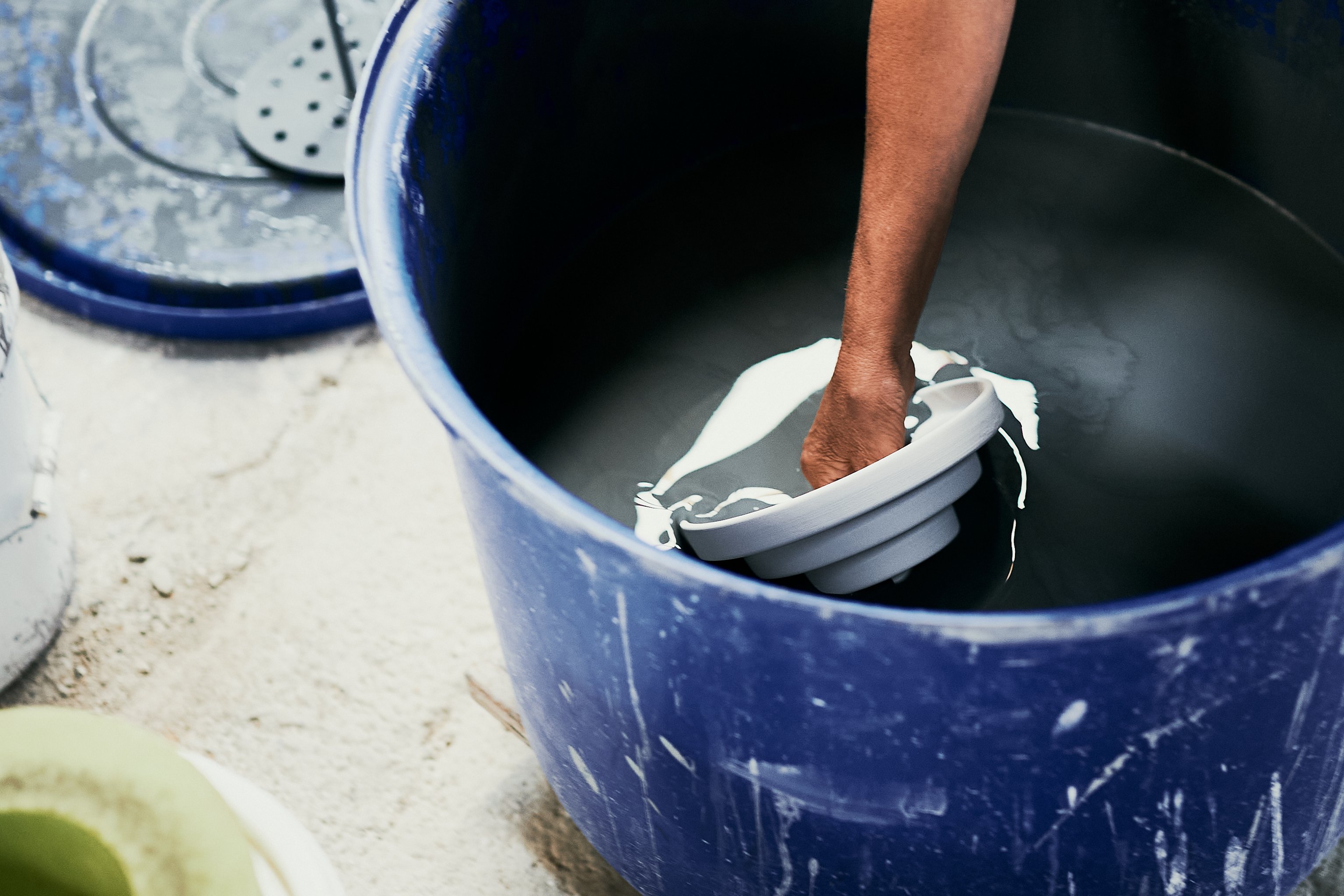 A ceramic Honey lighting component is hand dipped into a blue bucket of glaze.