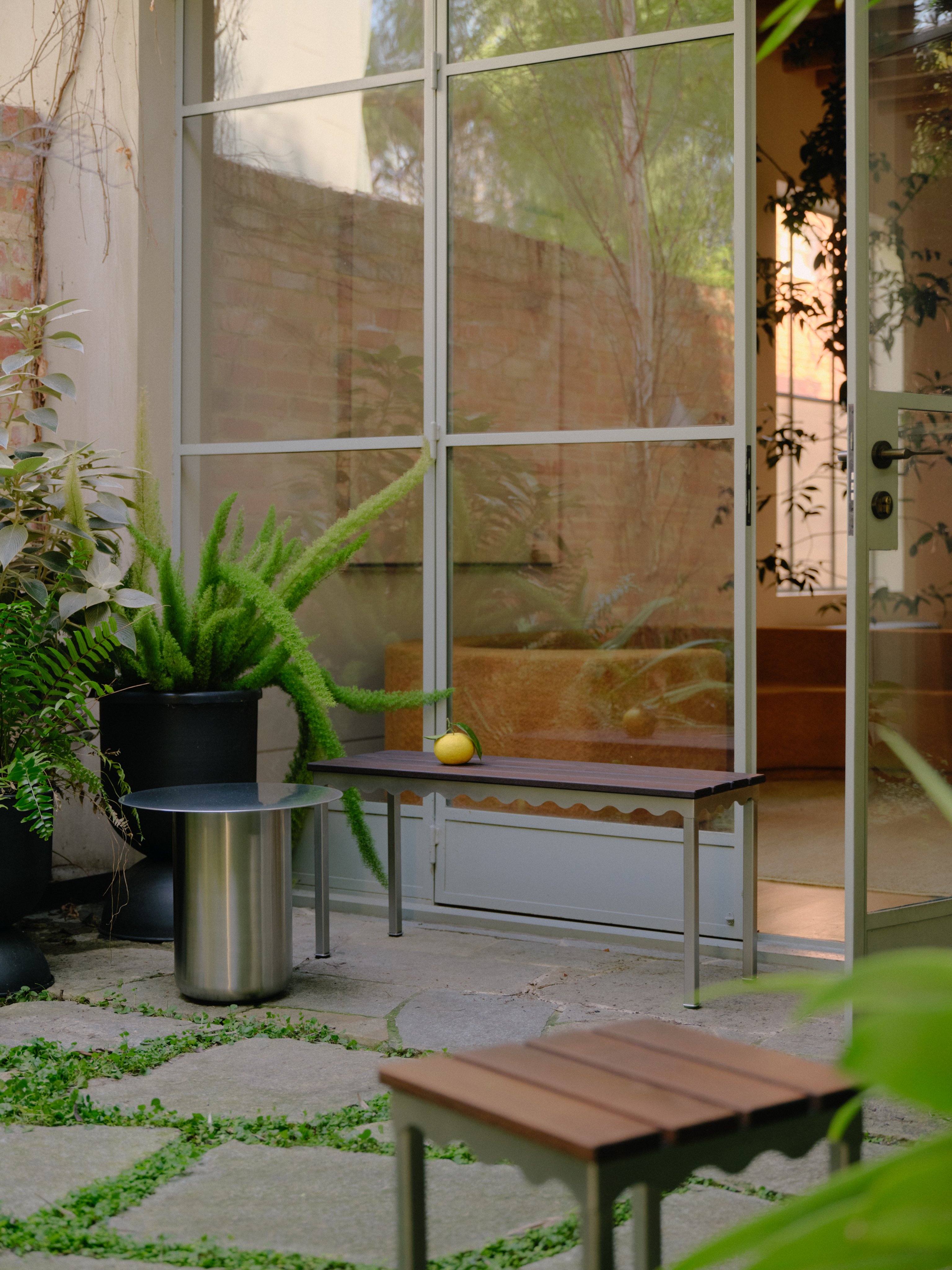 An outdoor courtyard with a stainless steel side table and a stainless steel bench seat and stool