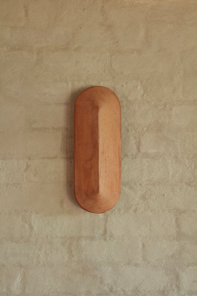 A Pinch 400 elongated wall light made of terracotta, against a white brick background
