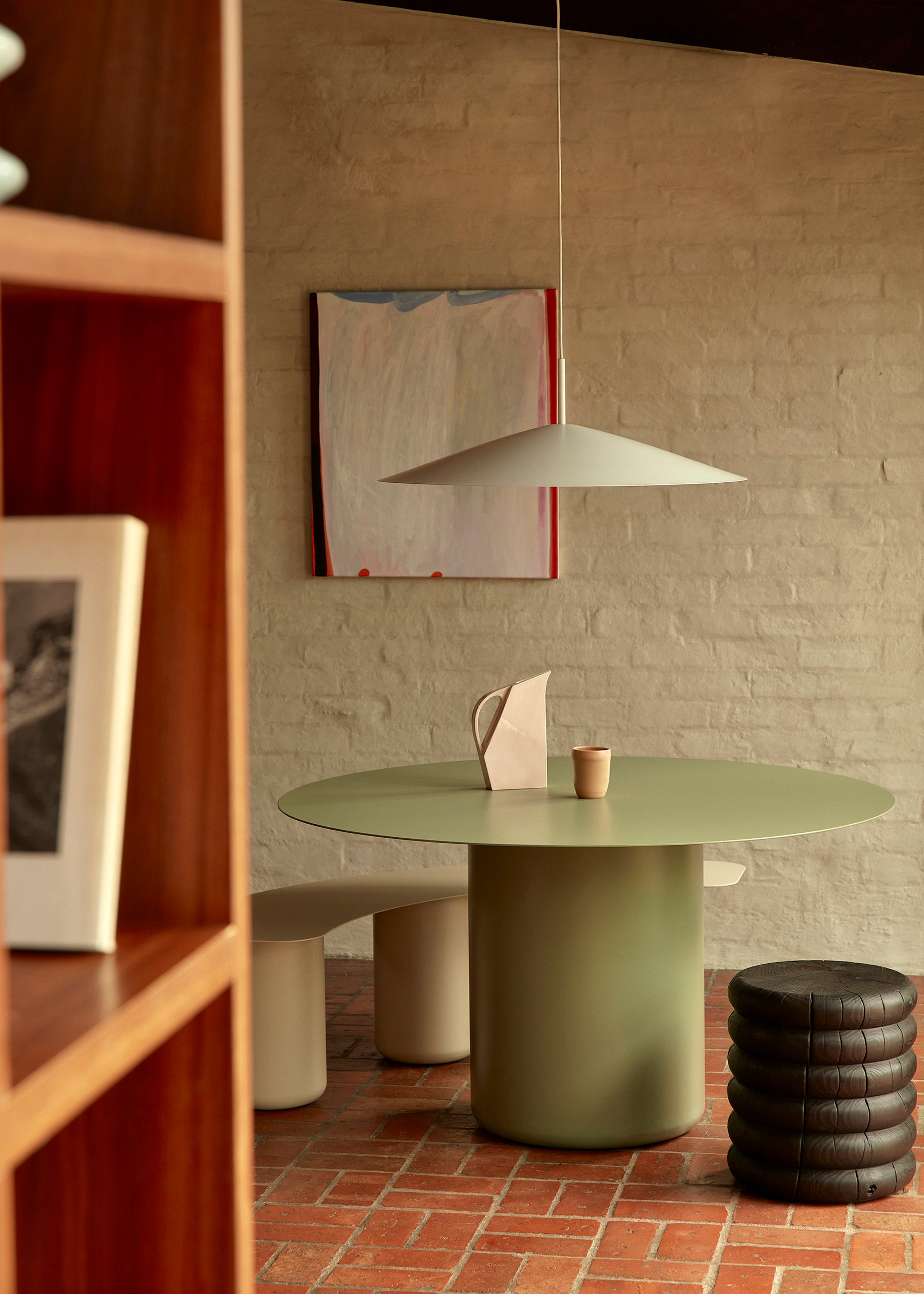 Green round dining table in a warm room with brick floor and rendered brick wall.