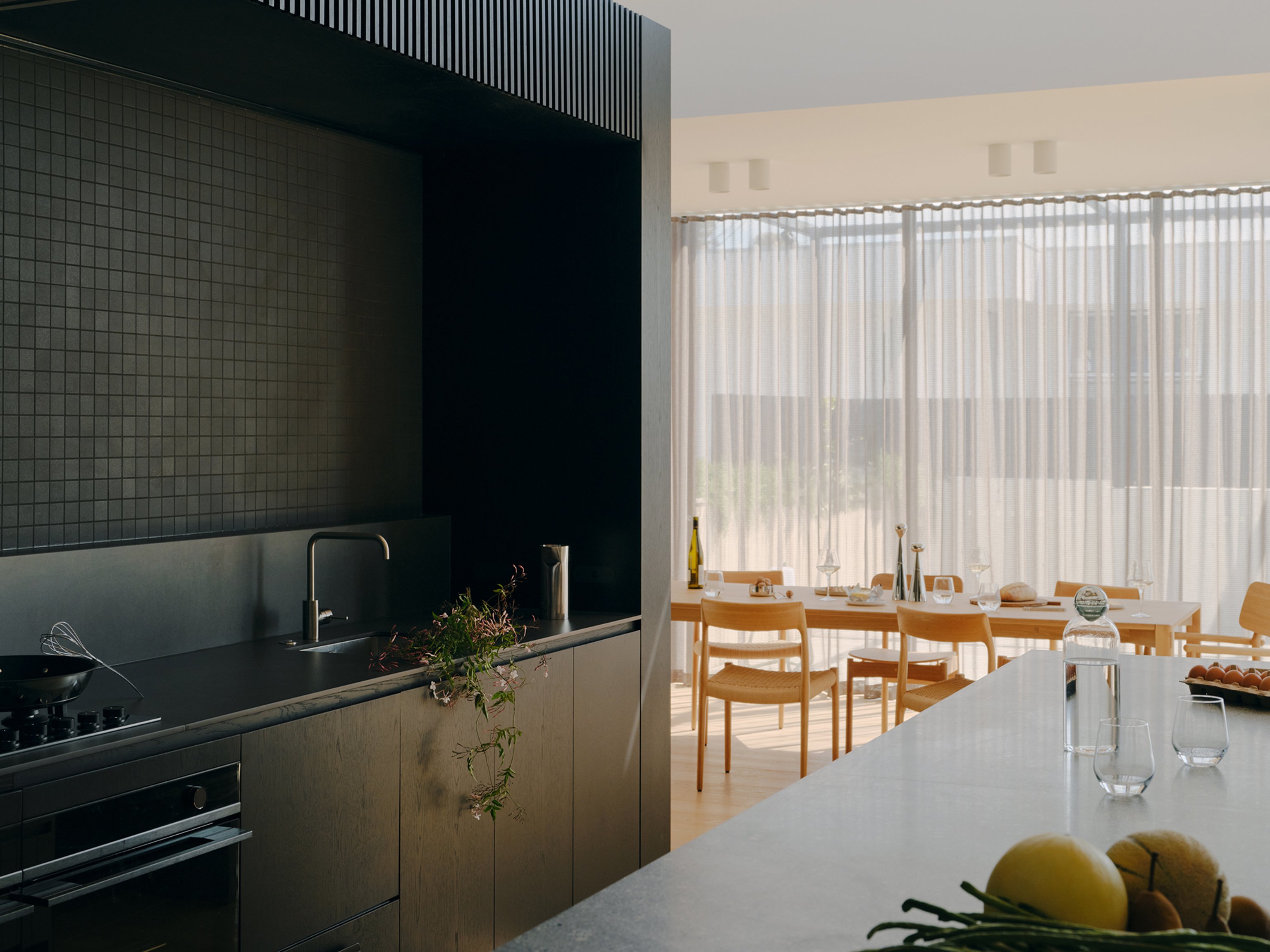 A black kitchen with light island bench and dining area