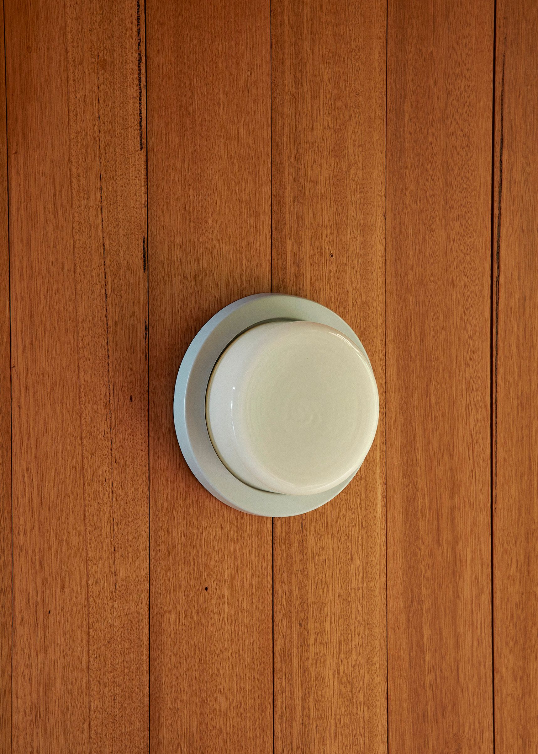 A single rimmed Honey Wall Light with a light blue ceramic slip-cast base and hand-blown glass diffuser