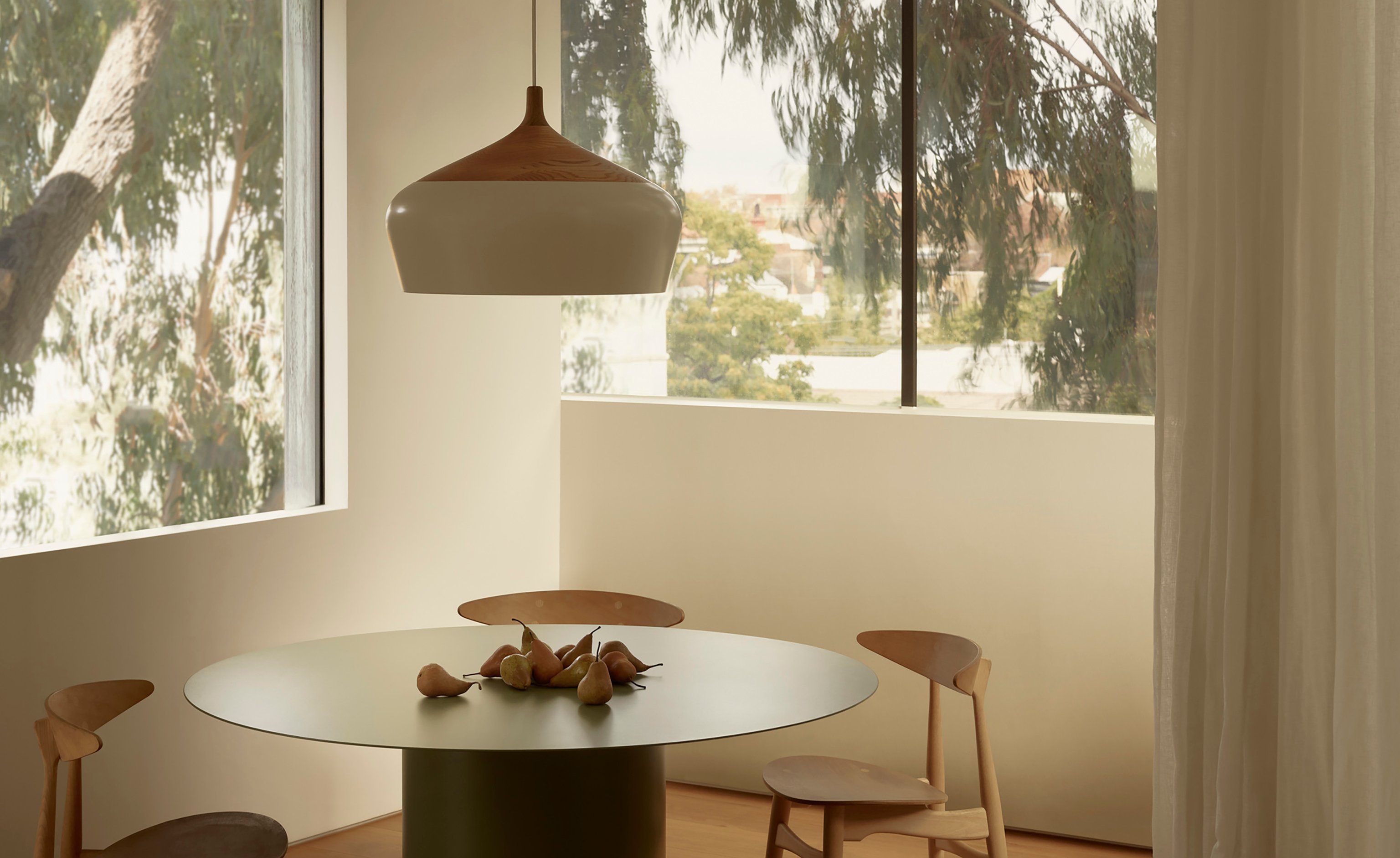 A dining room with a green rounding dining table and coco pendant