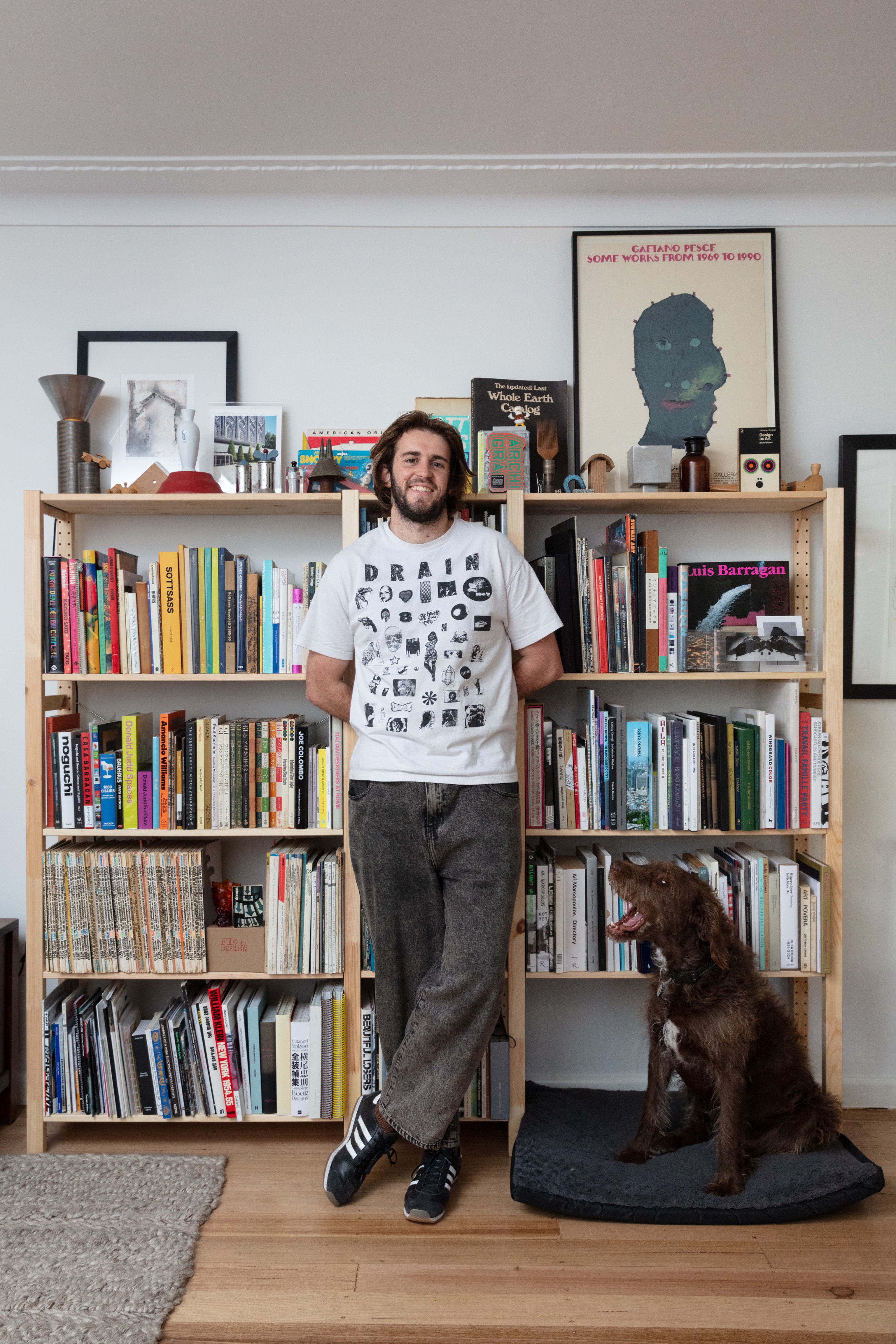 A portrait of Sean Brickhill, curator of First Edition Library, standing in front of a bookshelf with his dog Daisy.