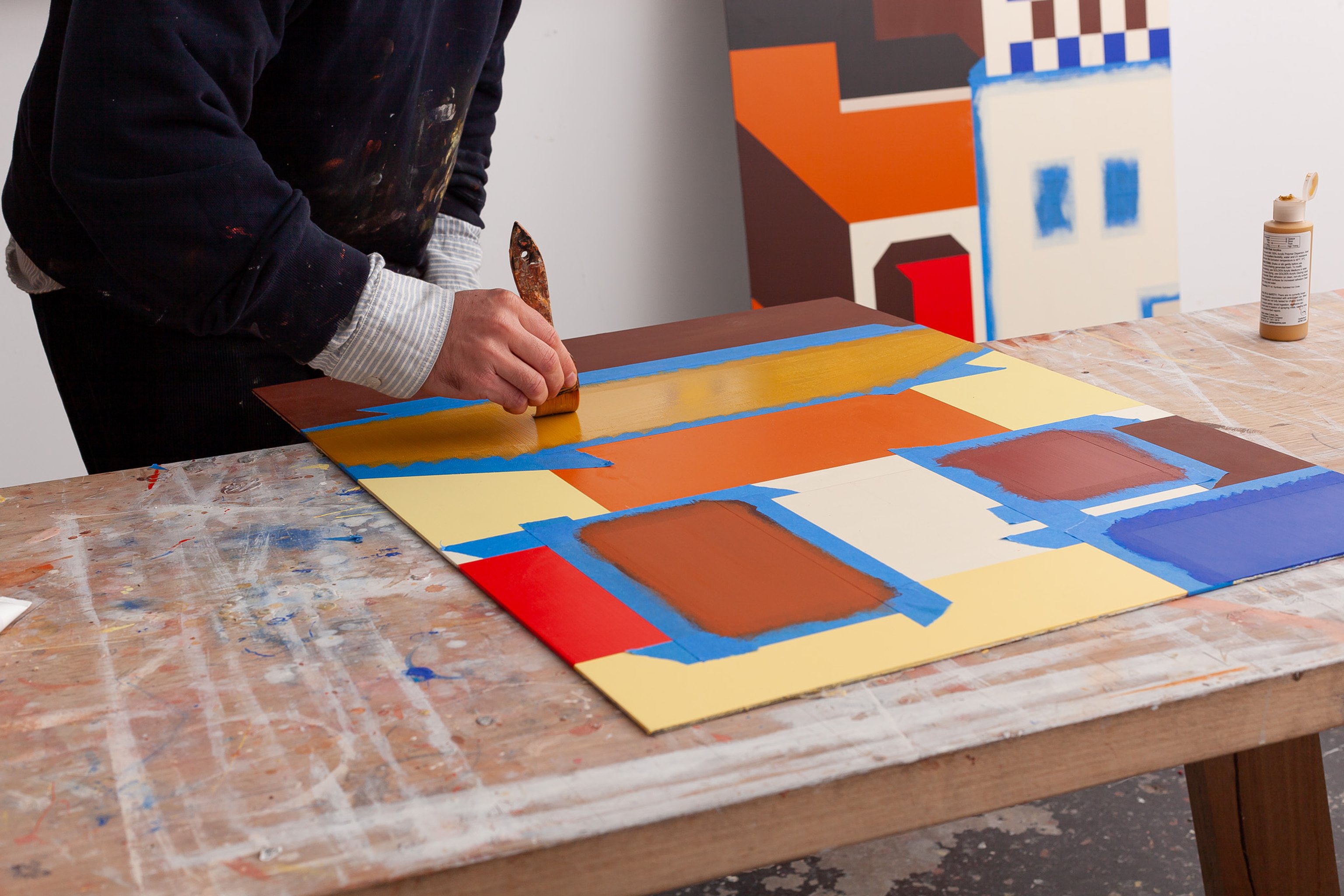 Mark Alsweiler working on a painting, consisting of browns, oranges, yellows and blue.