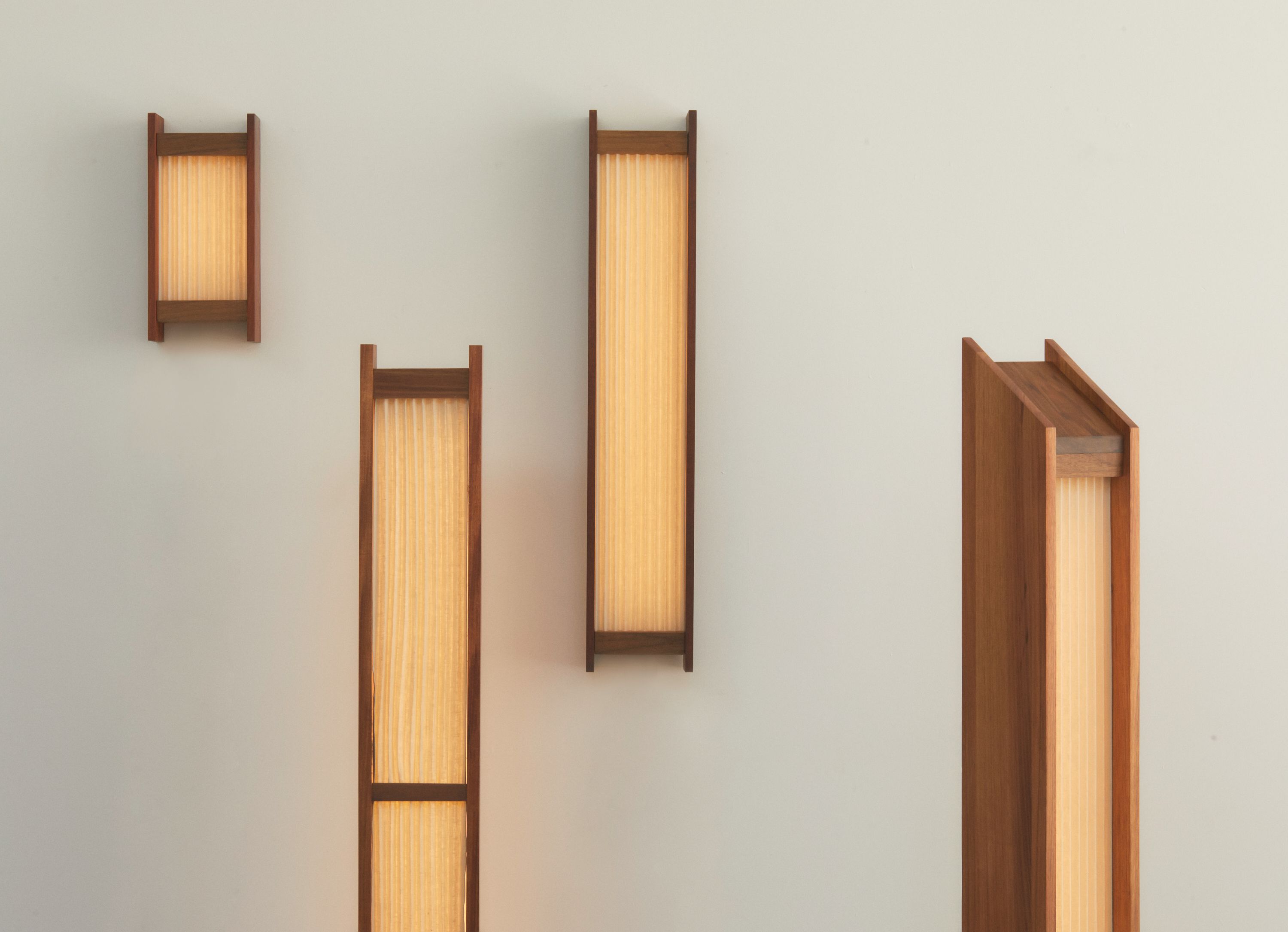 A collection of contemporary pleated linen light sculptures with timber base and warm glow, standing upright against a plain background.