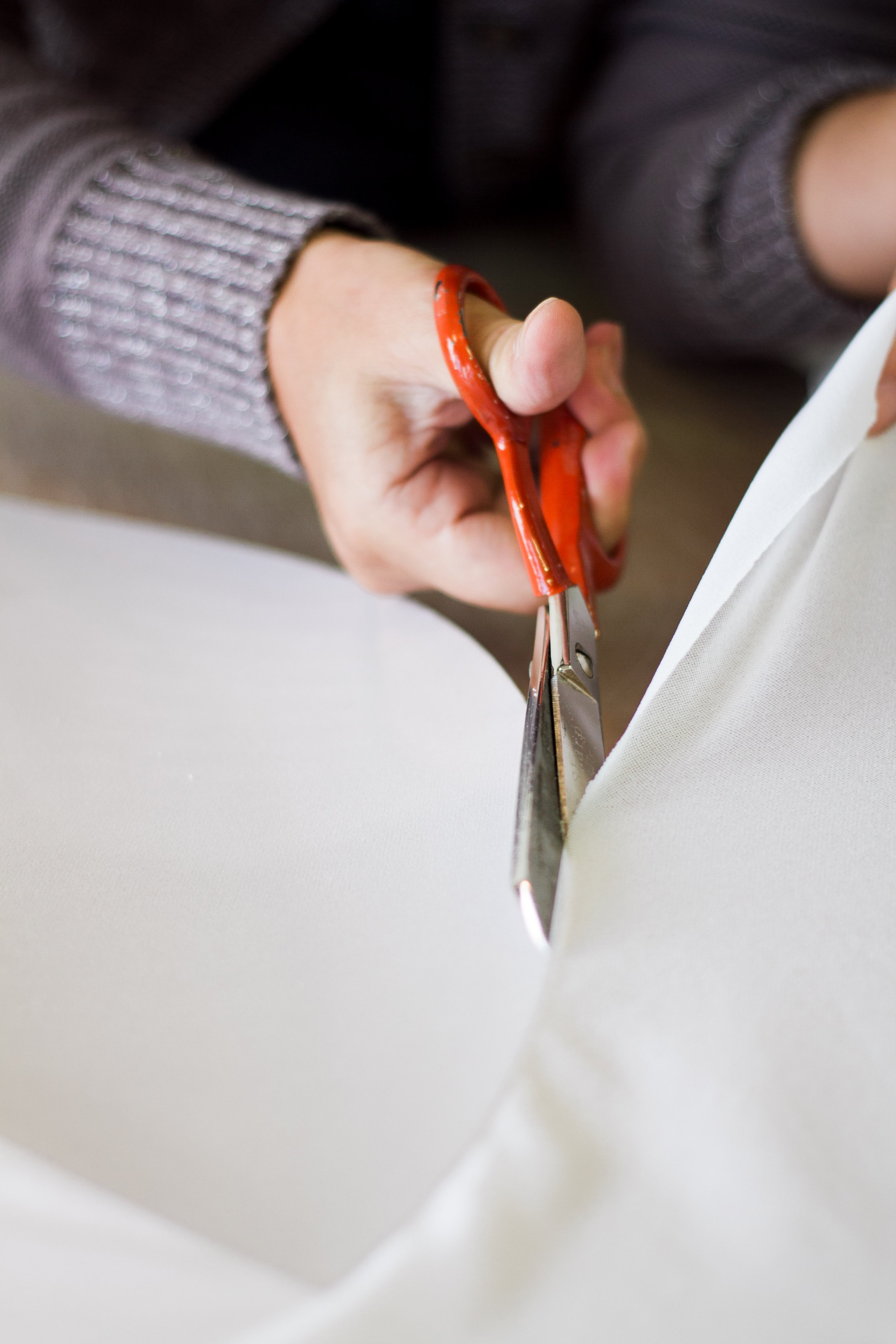 Hands using scissors to cut white mesh fabric to match a shape