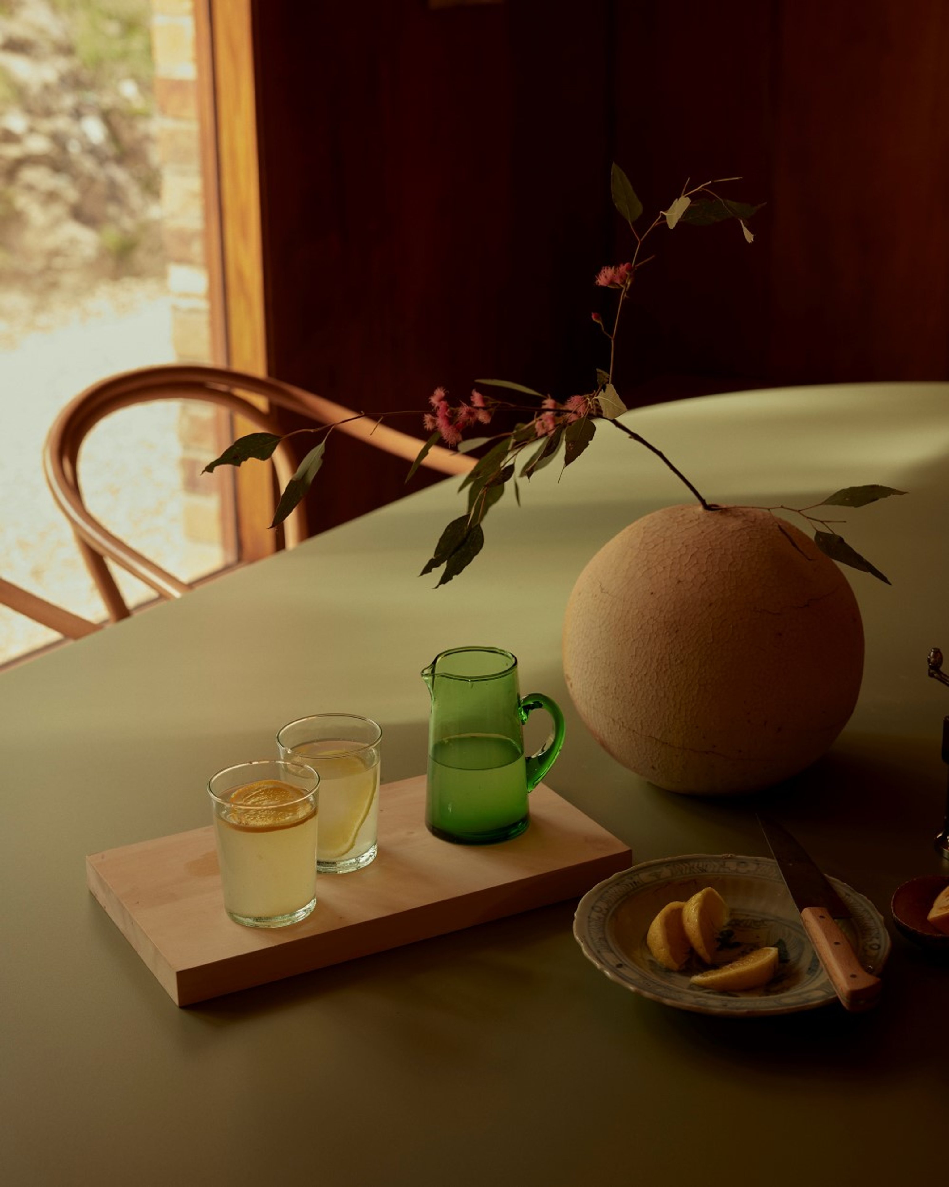 A green sequence dining table with two glasses and a jug of juice and sliced fruit on the table