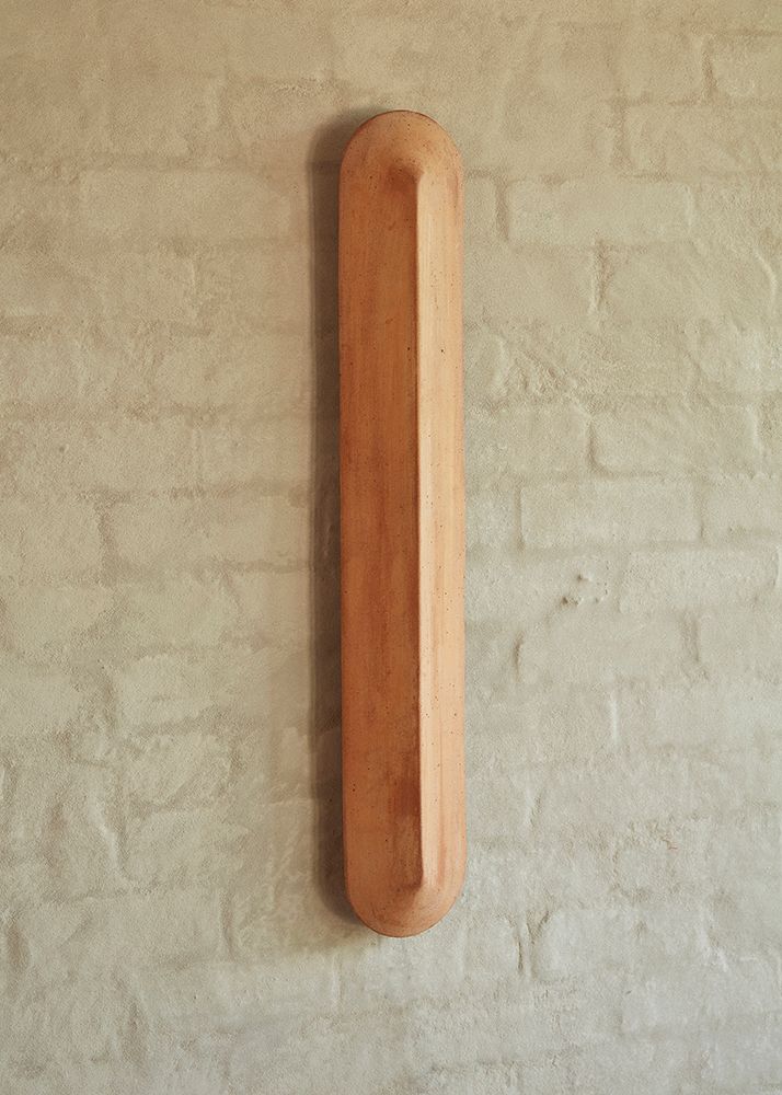 A Pinch 900 elongated wall light made of terracotta, against a white brick background