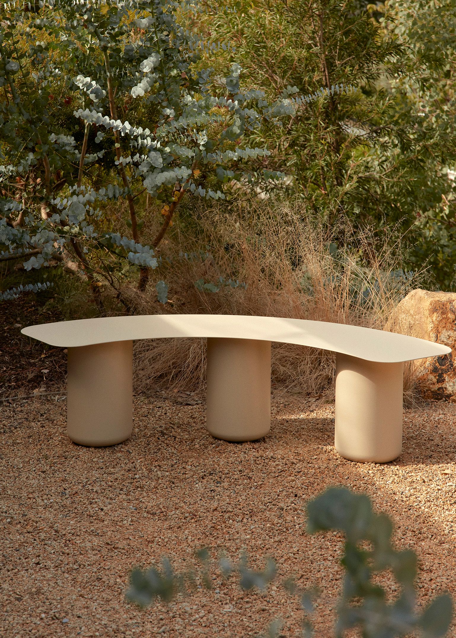 An outdoor seating area featuring a paperbark sequence curved bench seat and dense foliage..