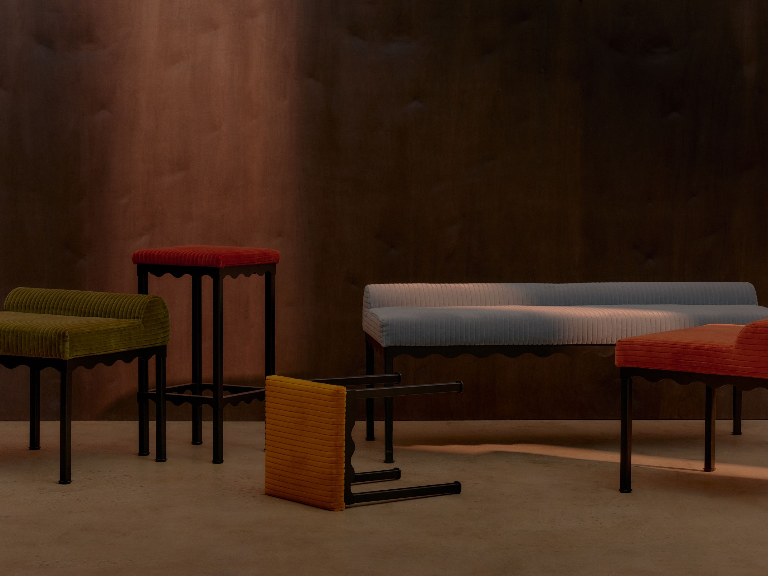 A collection of colourful upholstered bench seats and stools featuring wavy black metal frames